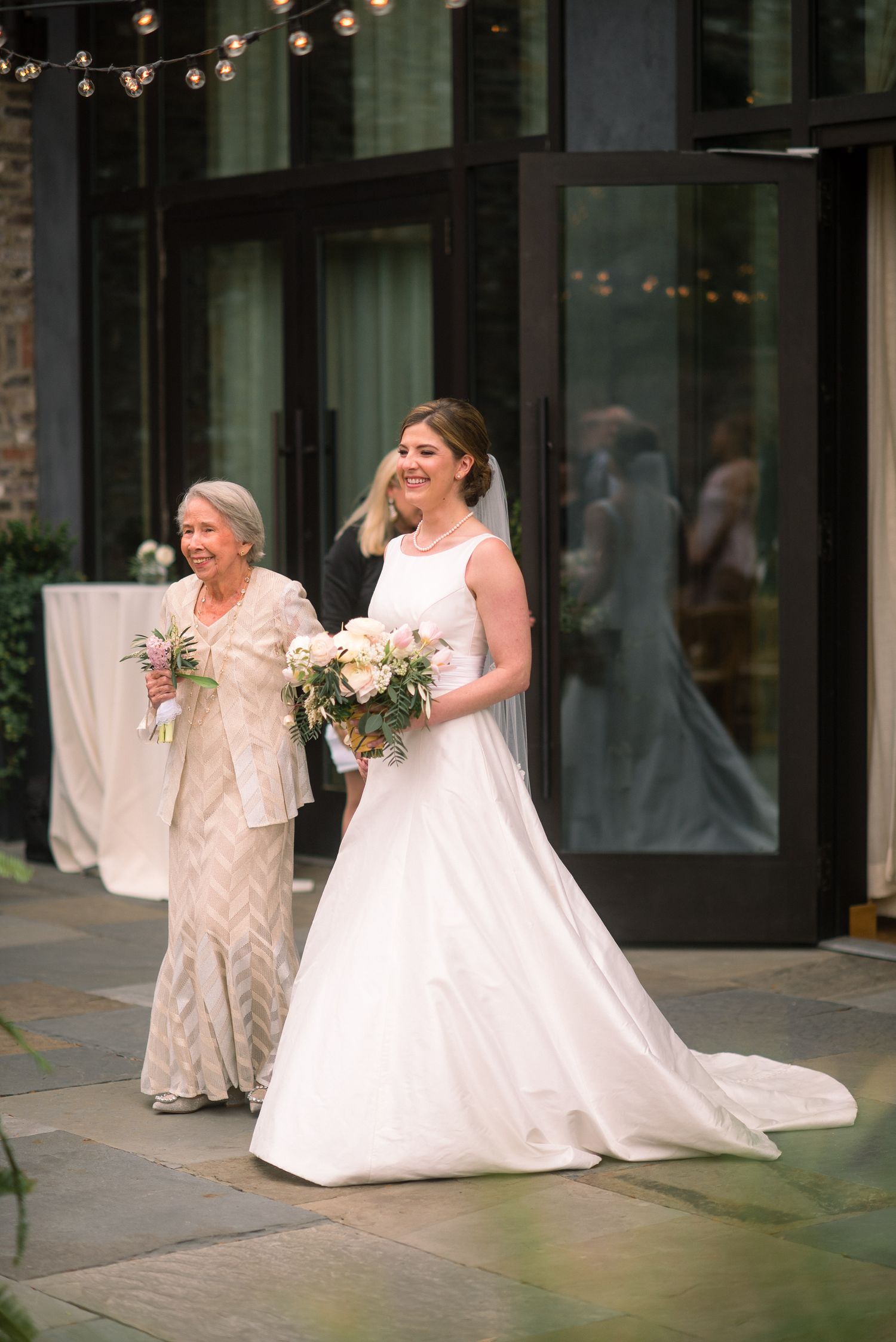 A sequence of four wedding photos showing a bride and companion walking and laughing together on a patio with string lights.