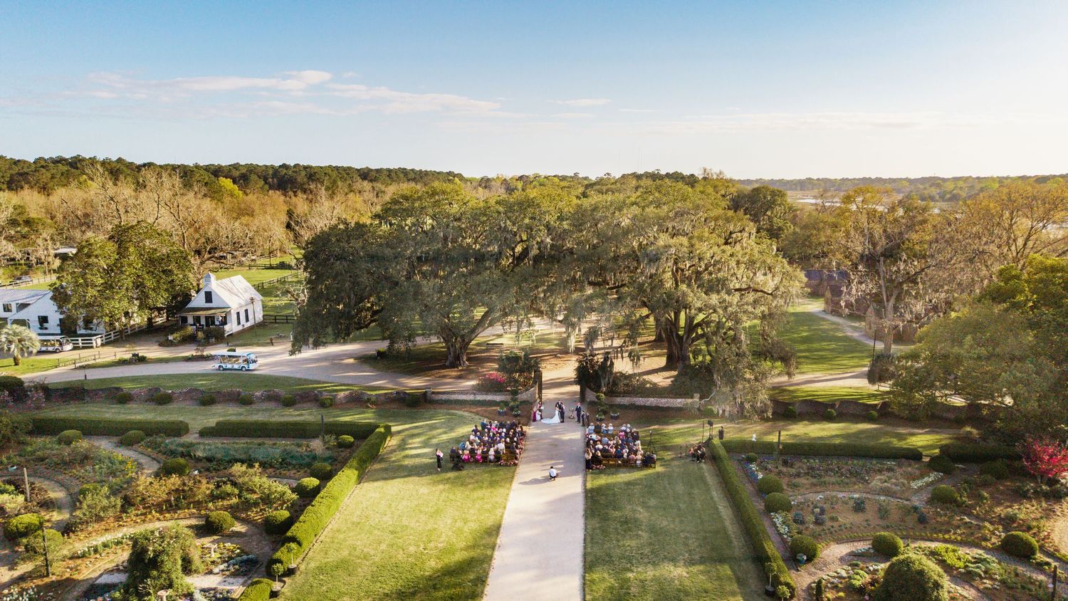 Panoramic aerial view of a lush golf course with rolling green fairways, trees, and winding cart paths under blue skies.