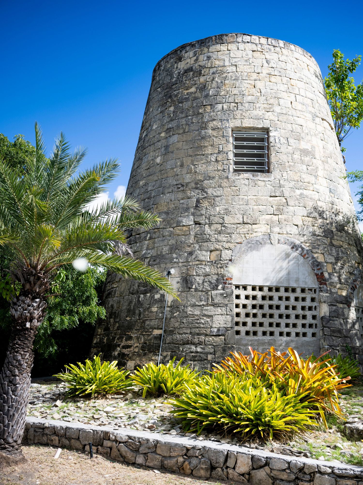 Series of white stone structures with tropical plants and landscaping along a curved wall.