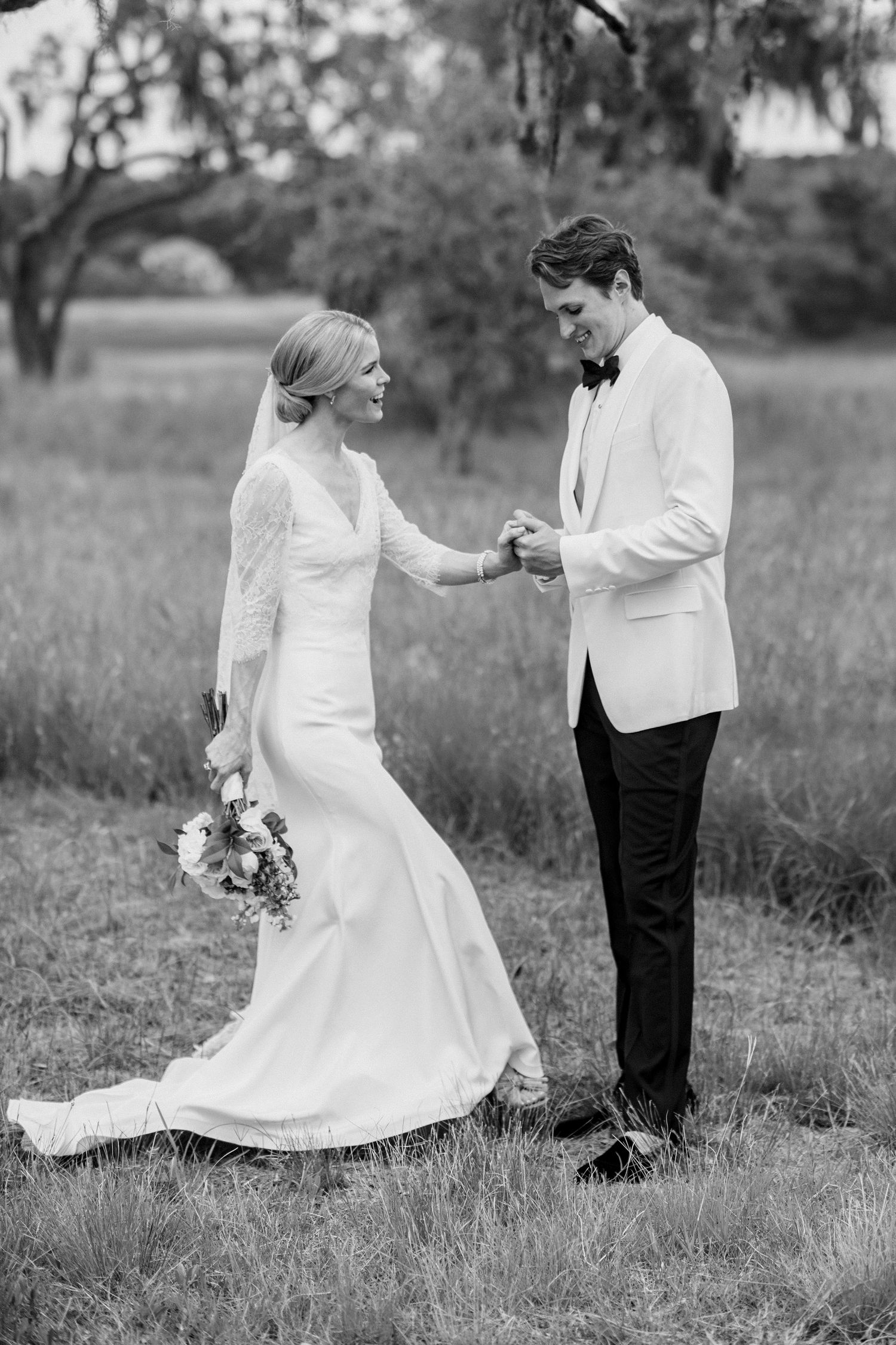 Black and white photo of couple dancing in field wearing formal attire.
