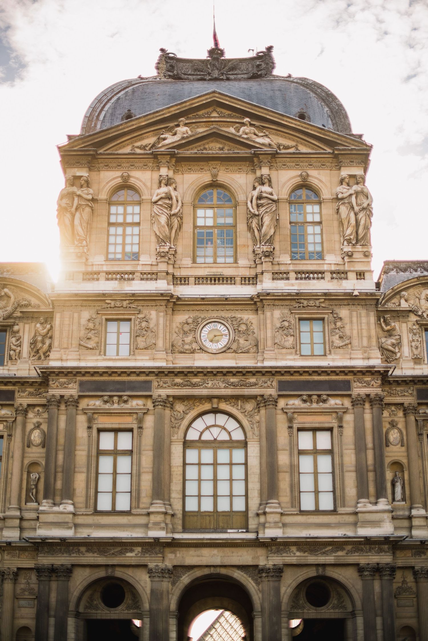 Ornate classical European building facade with decorative sculptures and grand windows in golden afternoon light.