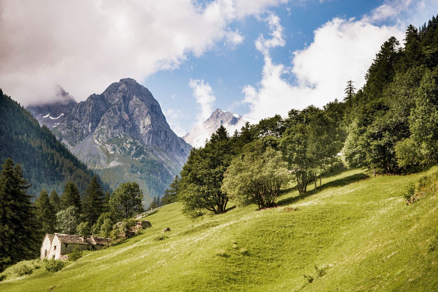 Panoramic mountain landscape on the road to Zermatt in Switzerland with green rolling hills and dramatic peaks under a blue summer sky.