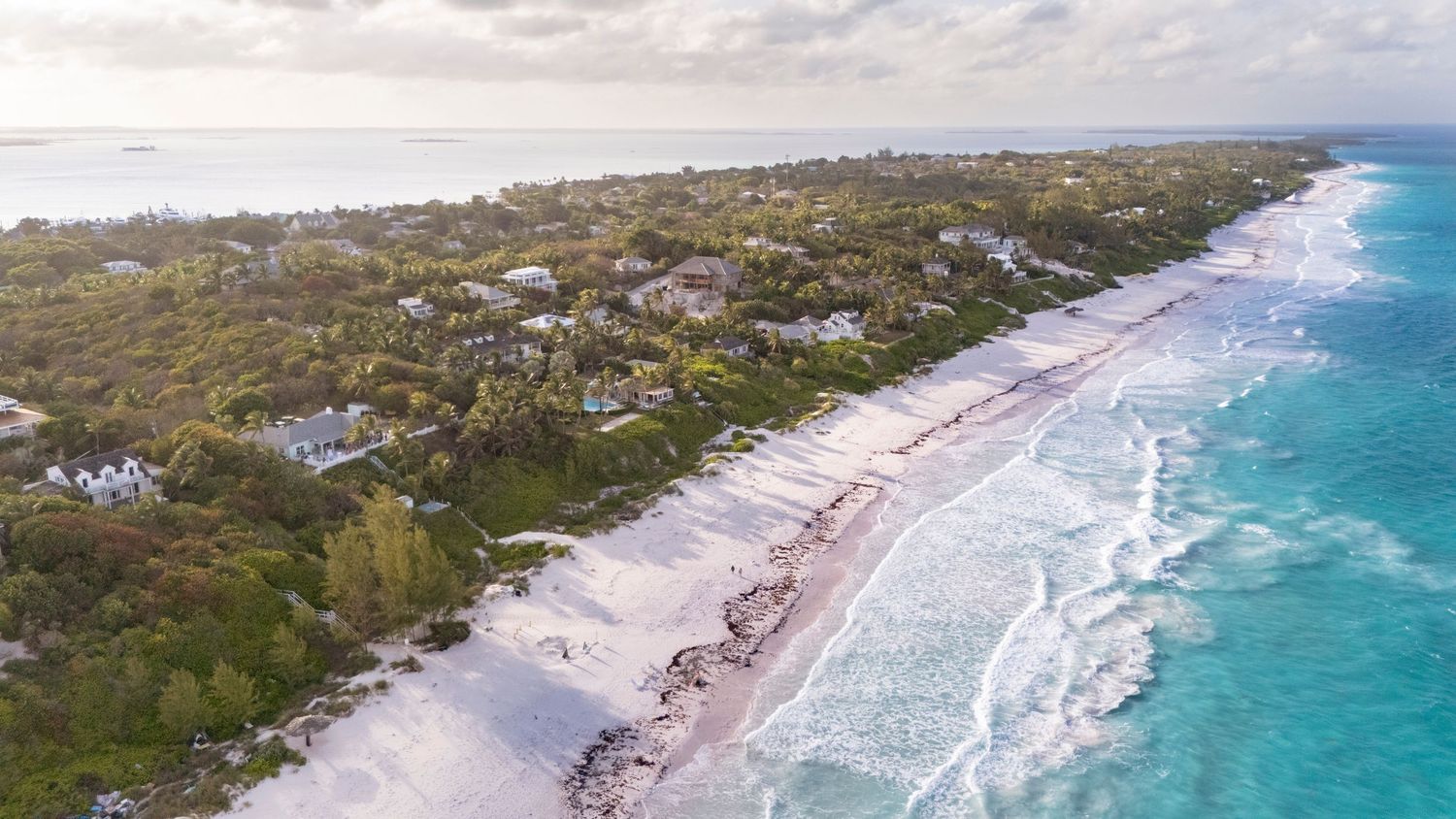 Aerial panoramic view of a pristine white sandy beach with turquoise waters and coastal vegetation in Australia.