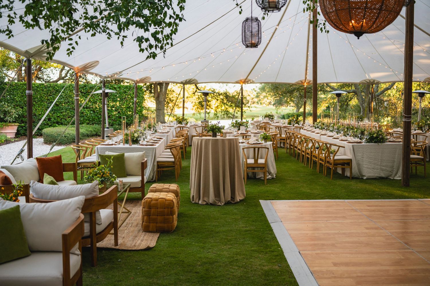 Elegant wedding reception setup under white tent with rustic decor, wooden dance floor and hanging globe lights.