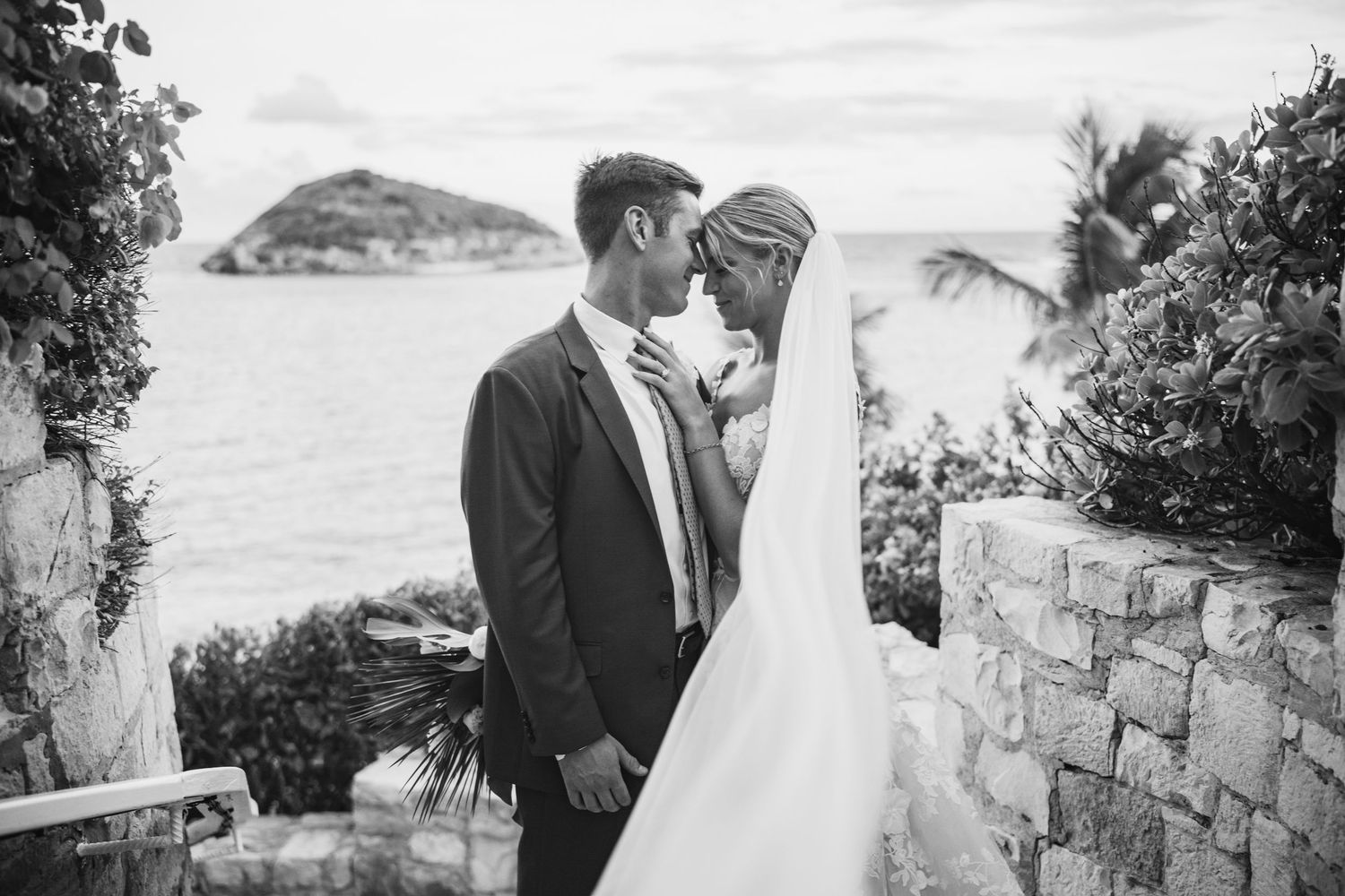 Wedding couple shares intimate moments against stone walls and tropical landscape.