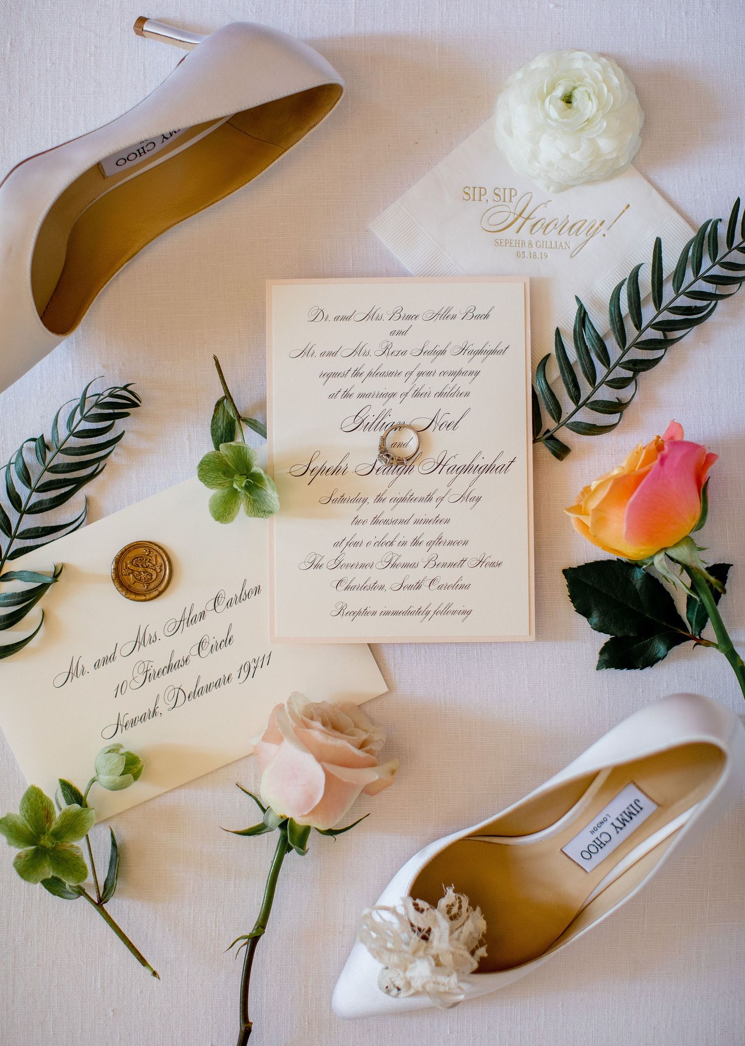 Wedding details flatlay with elegant invitations, white shoes, floral elements, and wax seals on a light background.