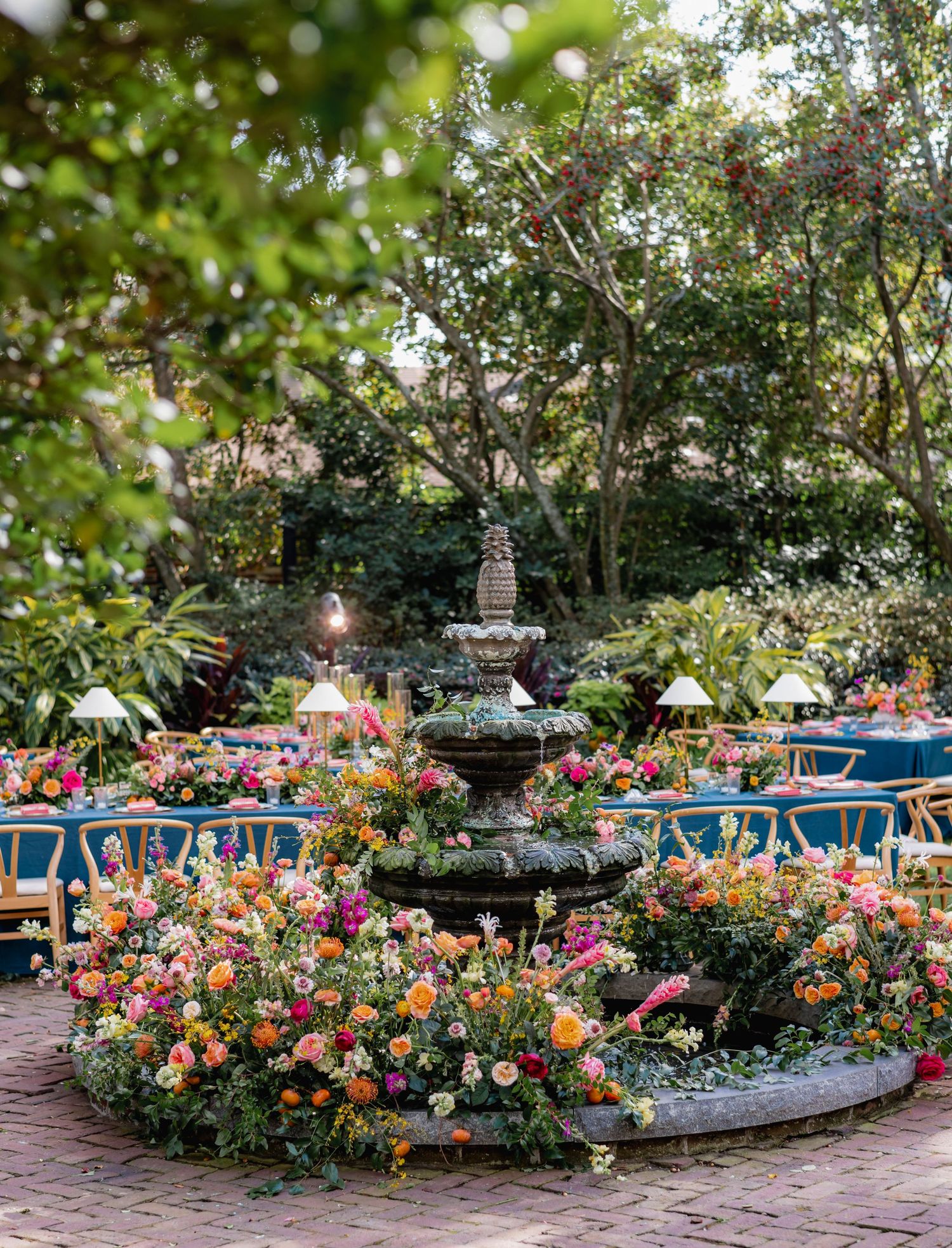 A lush garden fountain surrounded by vibrant pink and orange flowers with a blurred natural background.