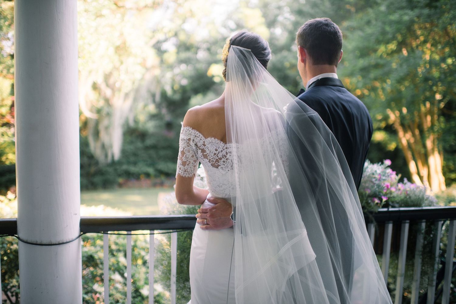 Bride and groom share an intimate moment together on a garden patio with white columns and greenery in the background.