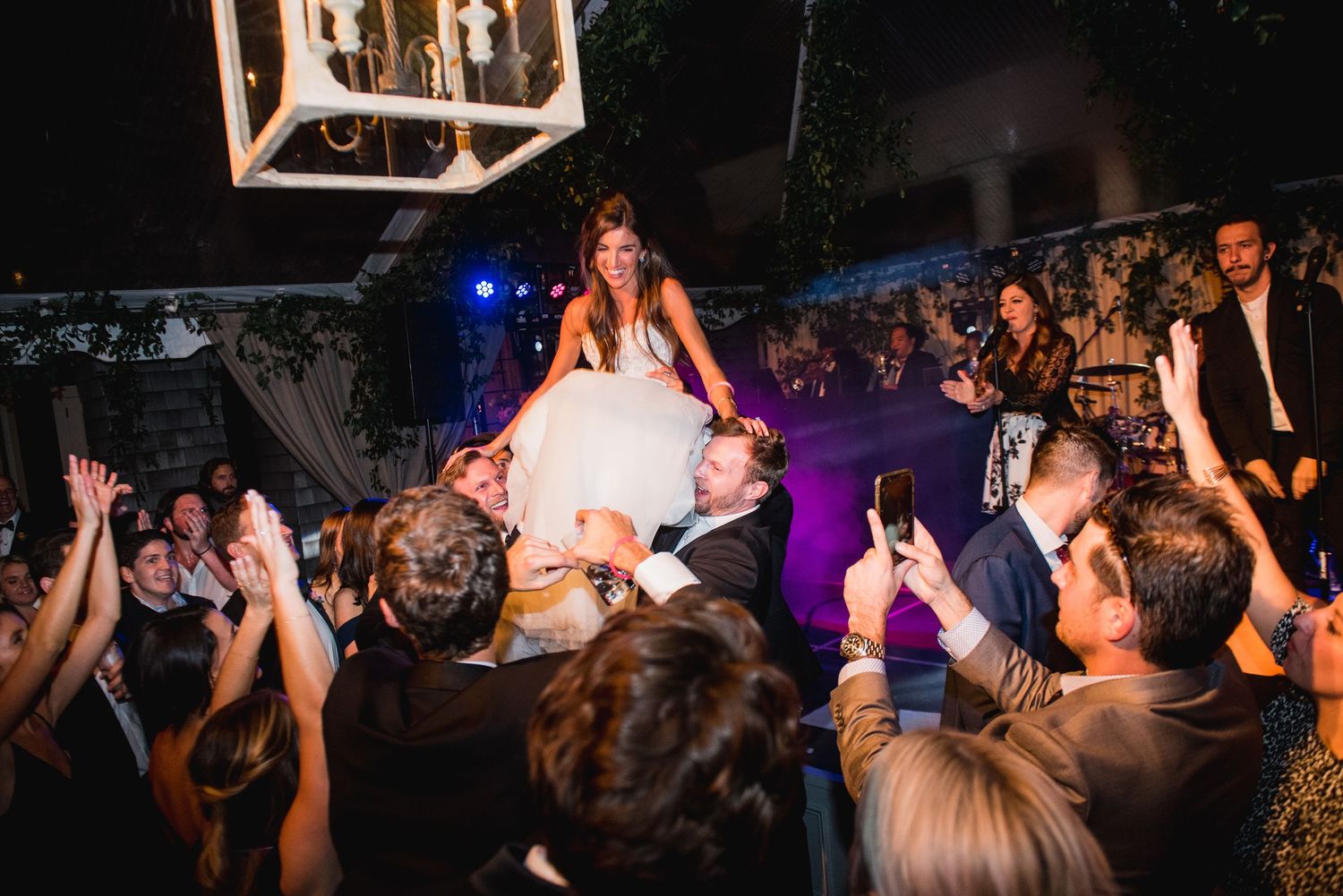 Energetic crowd at a wedding reception dancing and celebrating on a packed dance floor with colorful lighting.