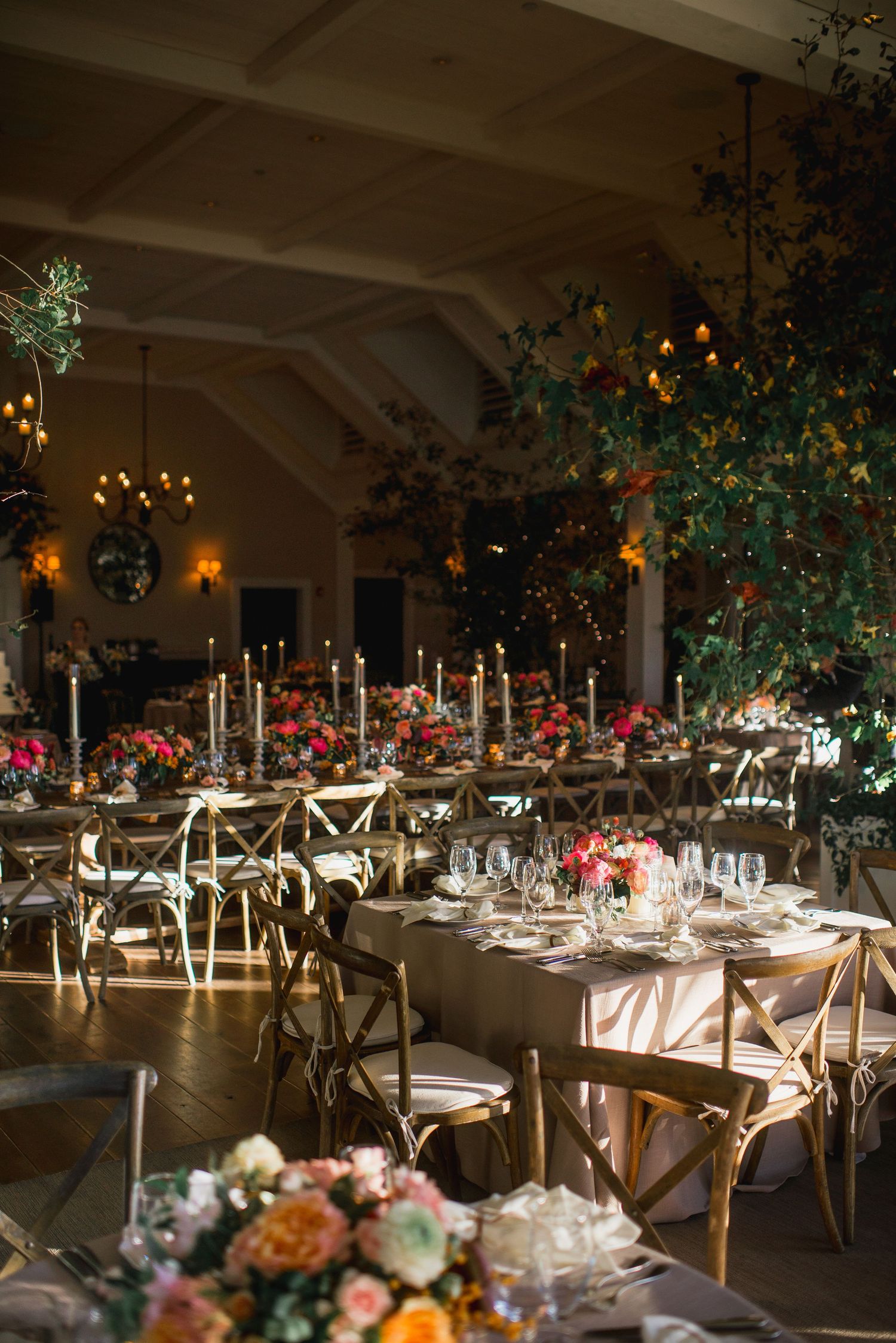 Elegant wedding reception venue with long tables decorated with floral arrangements and candles under warm lighting.