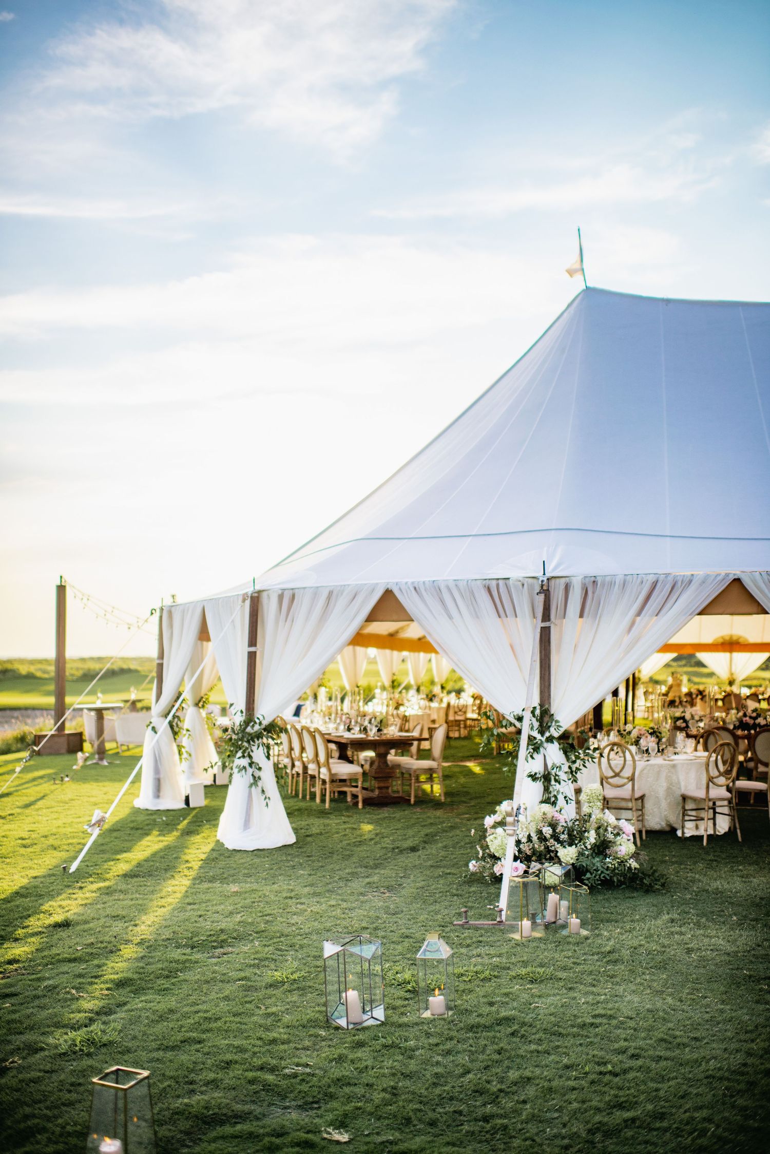Large white wedding tent reception setup on green grass lawn with elegant decor and tables at sunset.