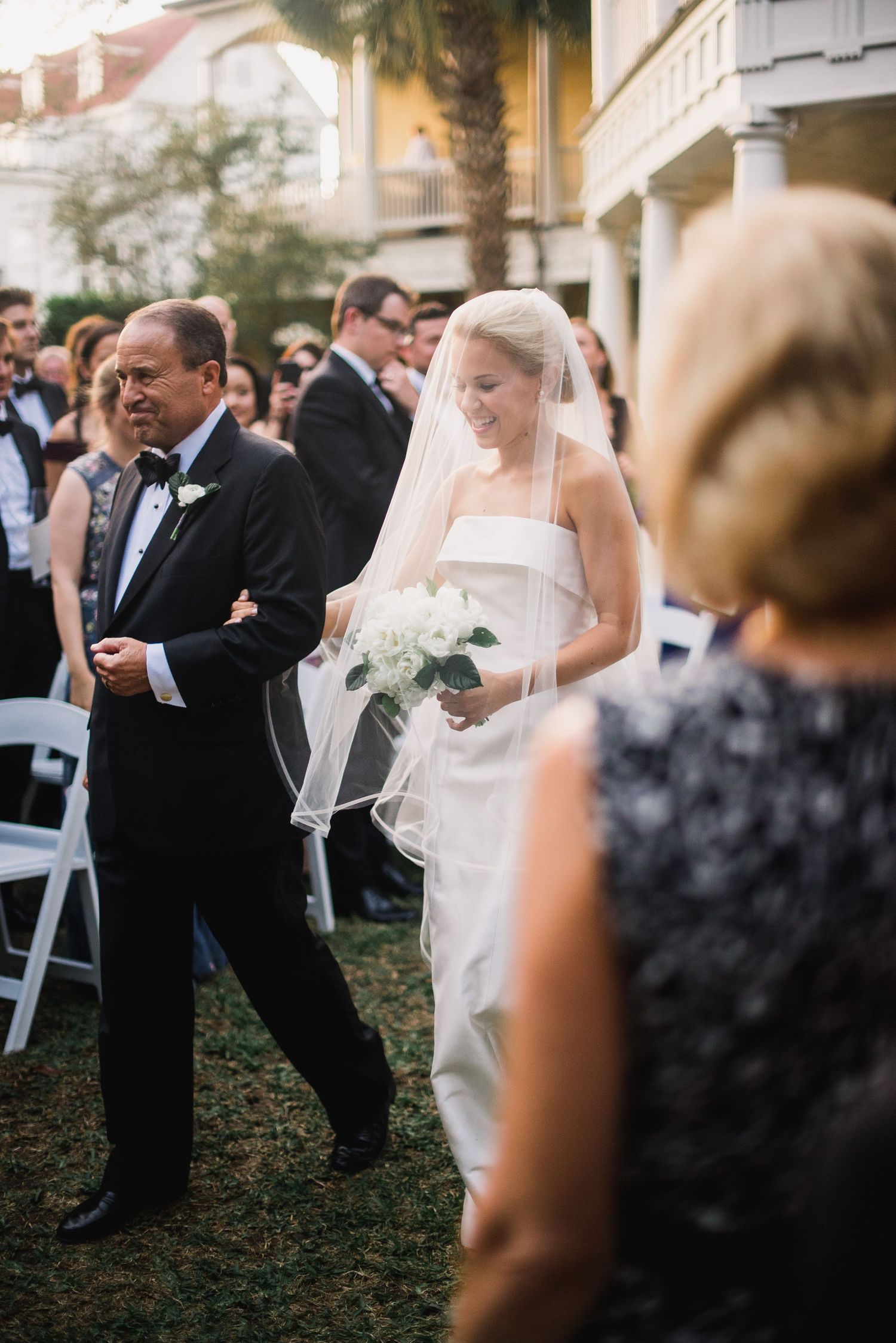 A sequence of wedding ceremony moments showing a bride and father walking down an outdoor aisle at dusk.