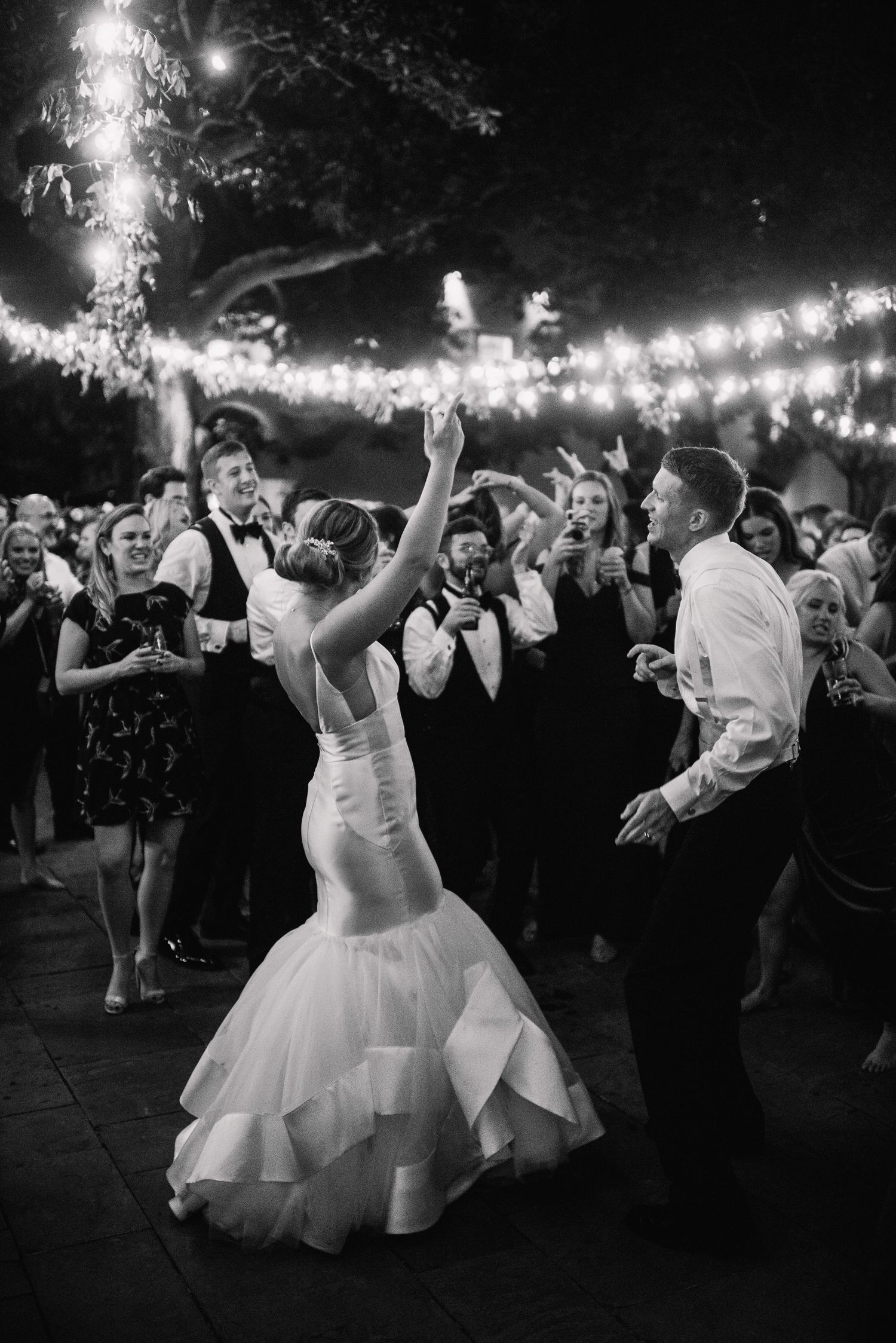 Black and white photos show a bride dancing joyfully at a wedding reception under twinkling lights.