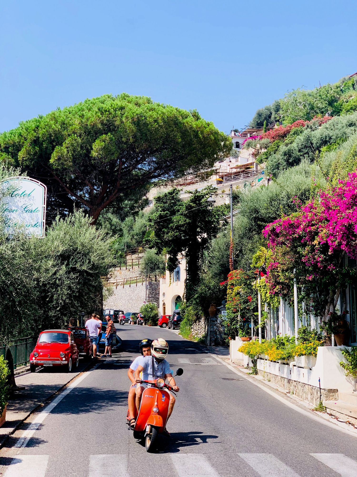 Scenic Mediterranean street lined with colorful bougainvillea flowers and stone walls on a sunny summer day in Amalfi coast italy