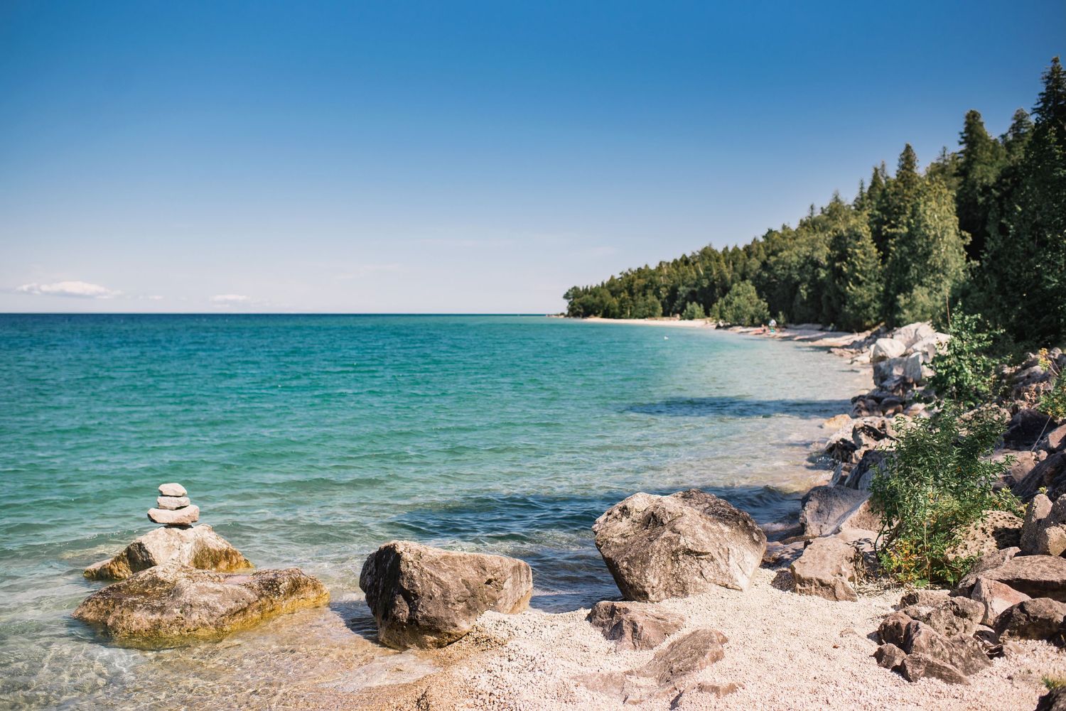 Rocky shoreline with crystal clear turquoise waters and pine forest along Lake Superior.