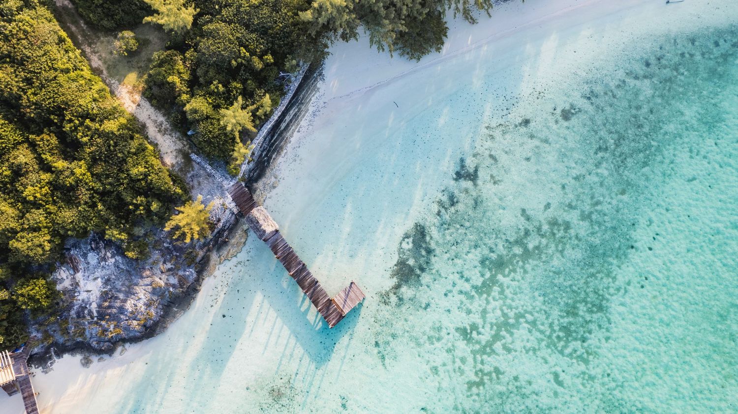Aerial view of crystal clear turquoise waters and wooden docks extending into a tropical lagoon surrounded by lush vegetation.