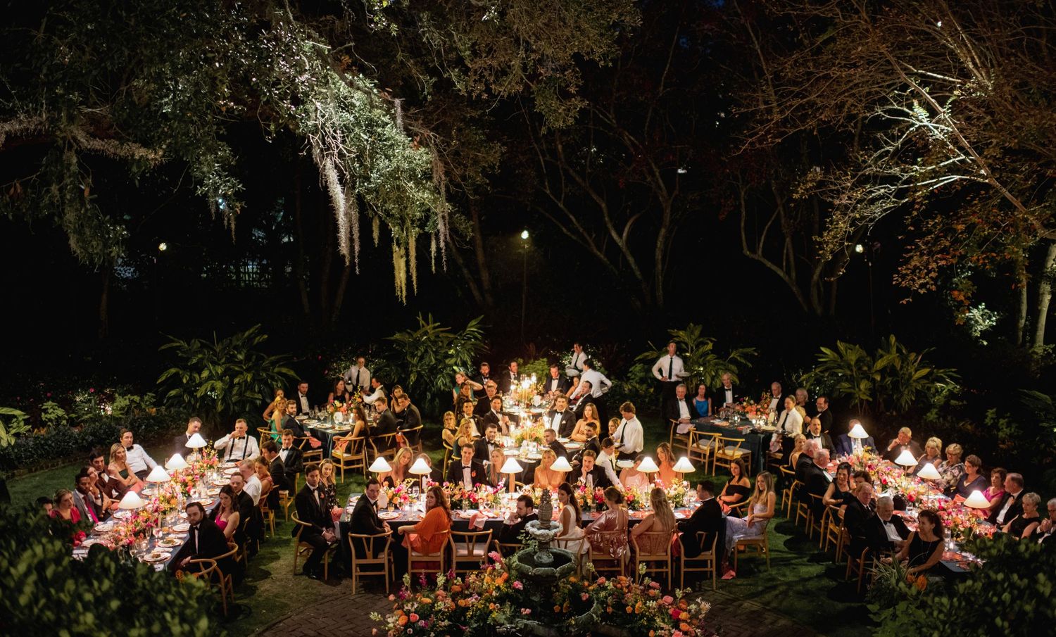 Outdoor wedding reception tables decorated with string lights and floral centerpieces create a magical garden atmosphere.