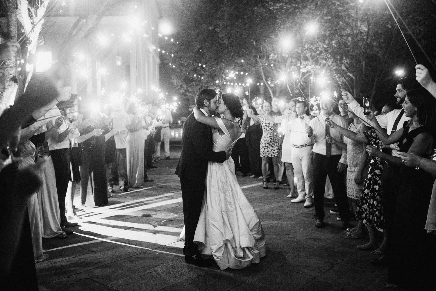 Wedding guests create a magical sparkler tunnel exit for the newlyweds at an evening outdoor celebration.