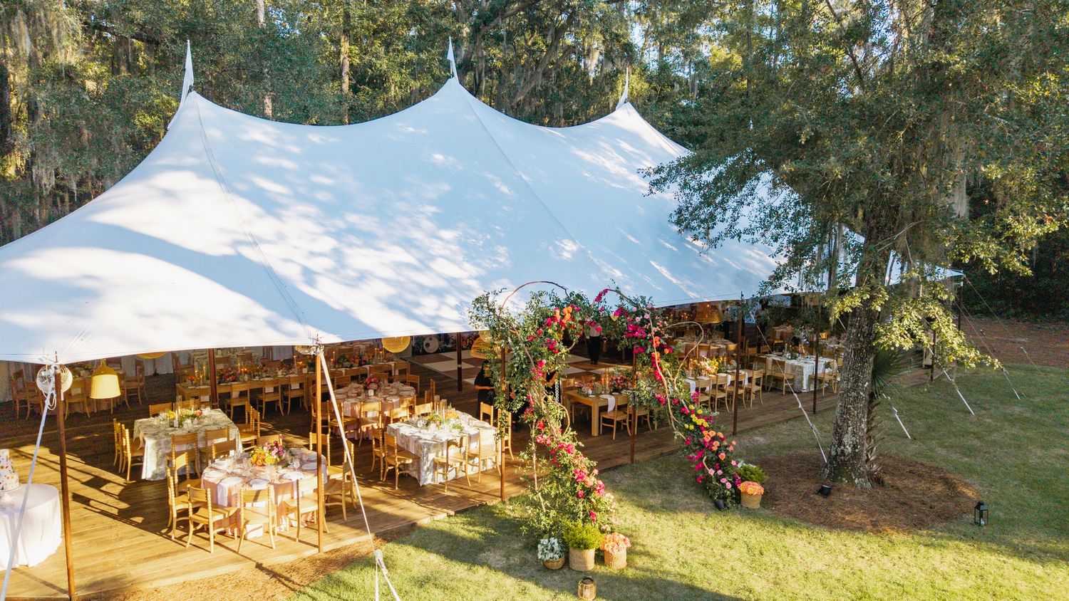 A panoramic view of an outdoor wedding reception setup with white tents, tables and chairs on a grassy lawn.