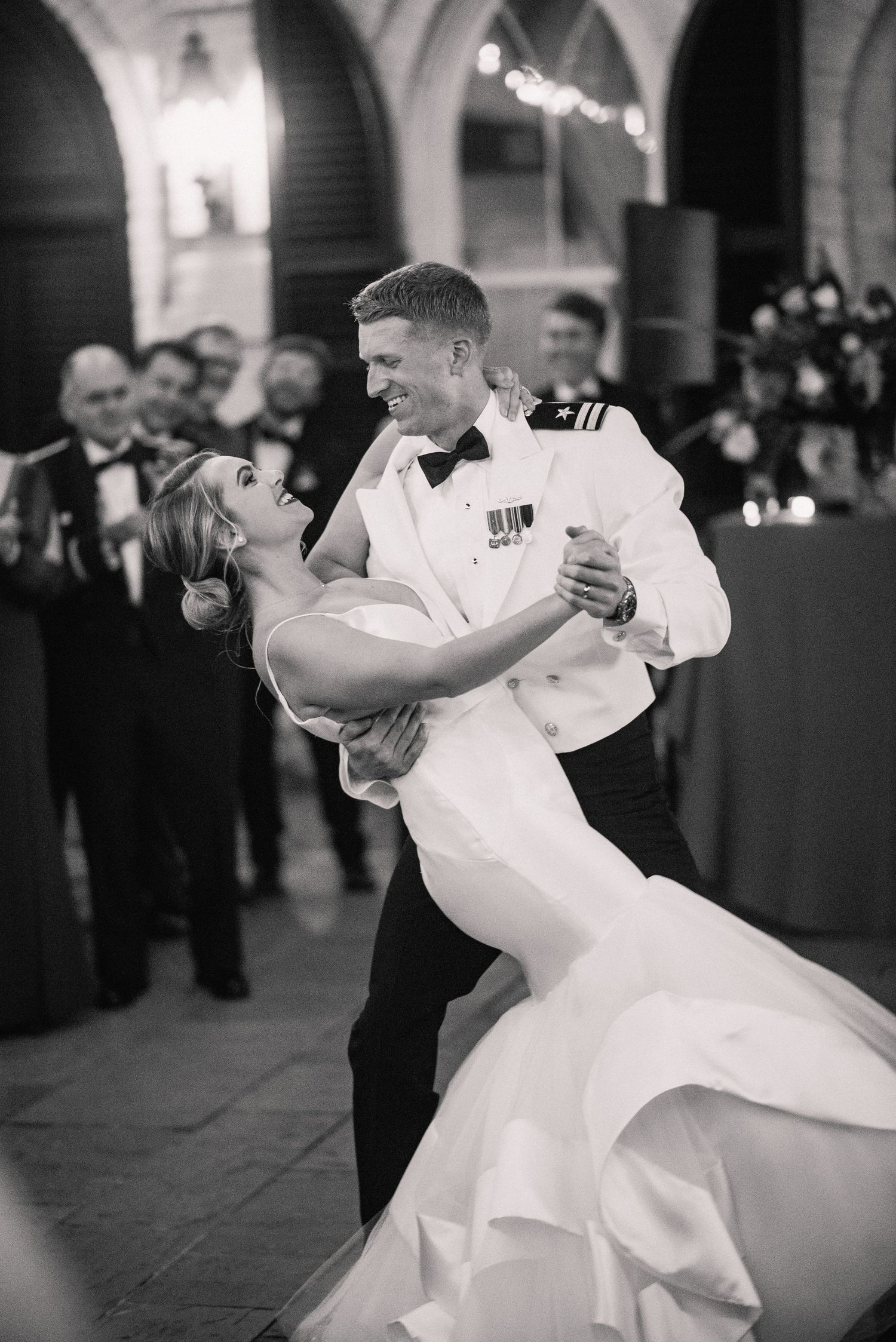 A couple shares a romantic dance at a formal military wedding reception, with the bride in white and groom in dress whites.