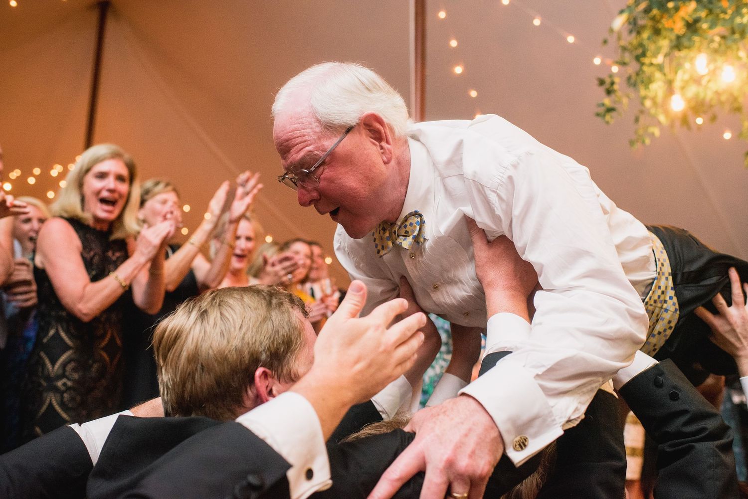 Wedding guests dance and celebrate joyfully on a dance floor under warm lighting at an indoor reception.