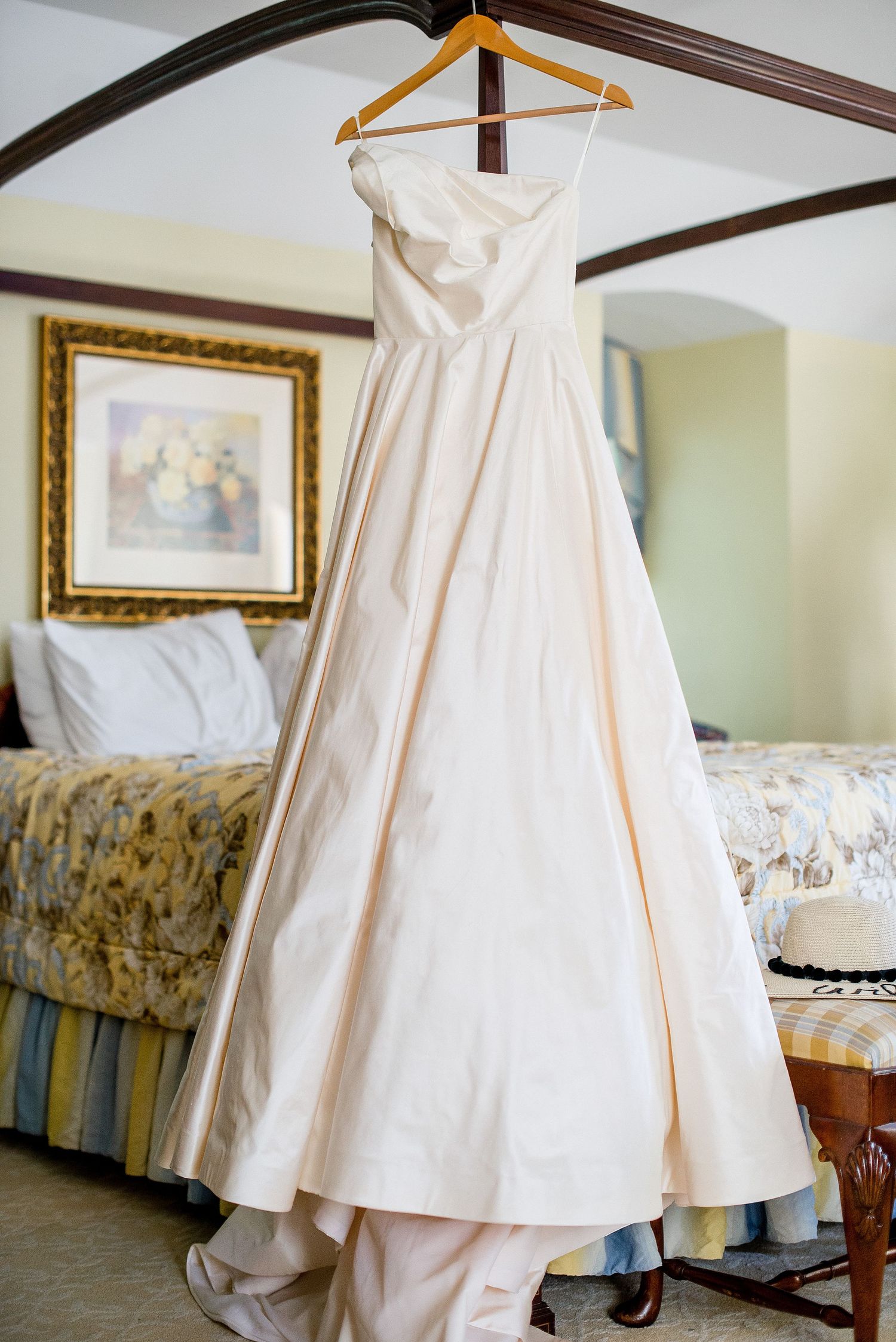 Wedding dresses hanging on hangers in a bedroom with floral bedding and traditional decor.