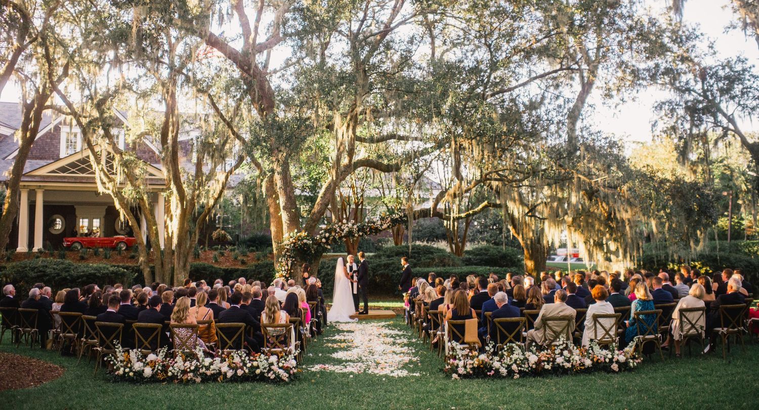 Large group of people gathered outdoors under shady trees for a special event on a sunny day.