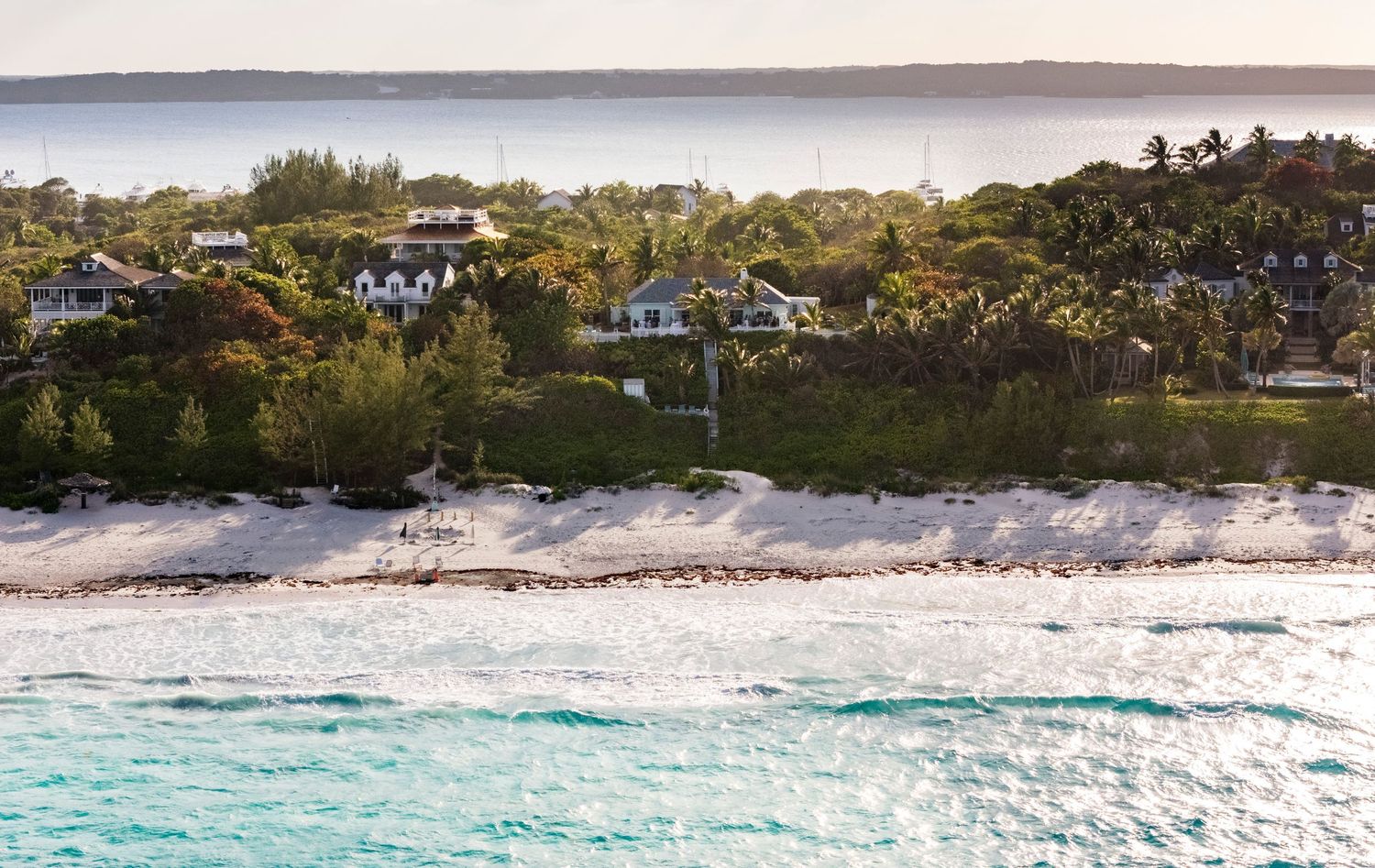 A panoramic view of a tropical beach with turquoise waters, white sand, and coastal homes along the shoreline.