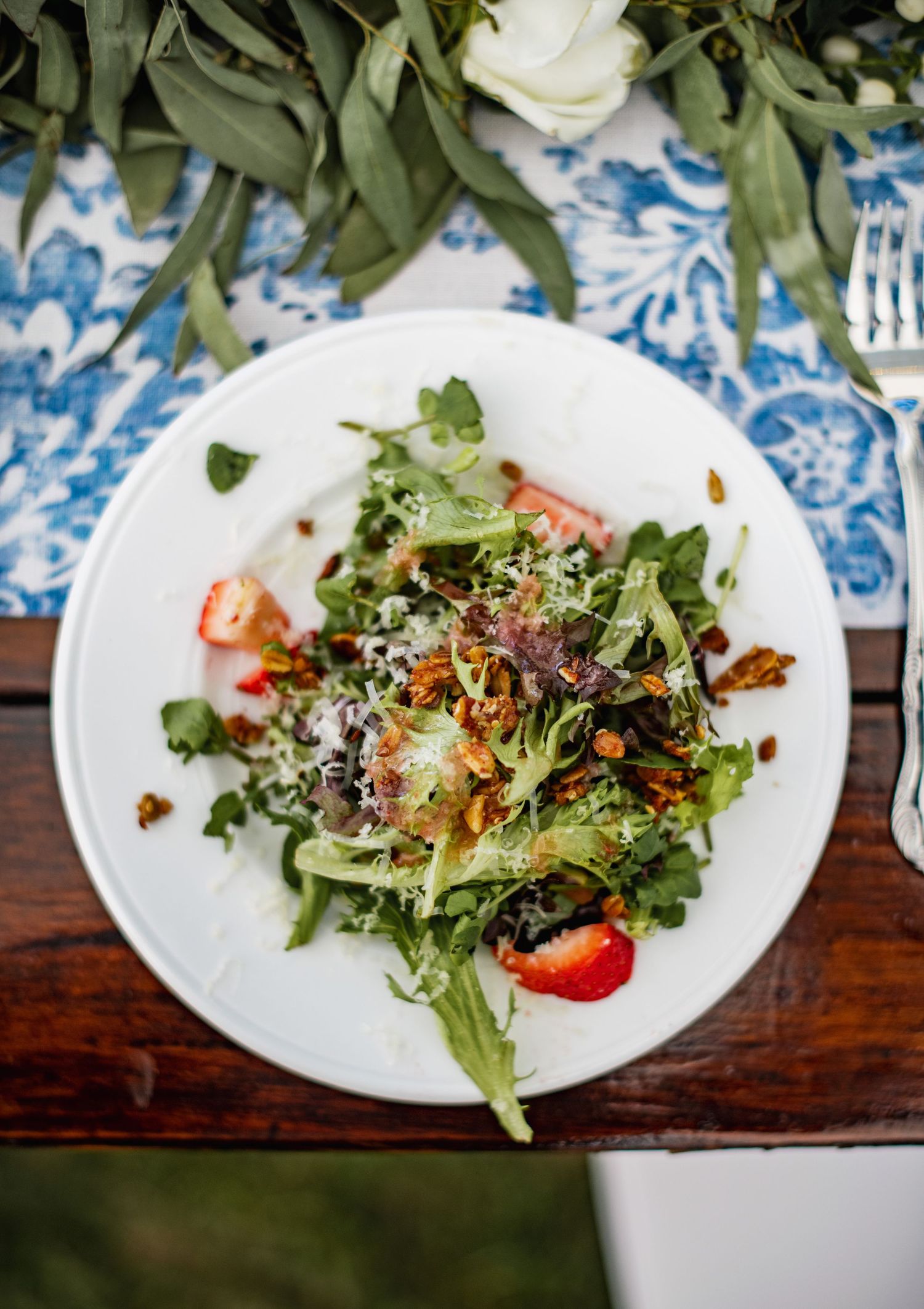 A sequence of plated salads with fresh greens, tomatoes and garnishes on a rustic wooden table with blue decor.