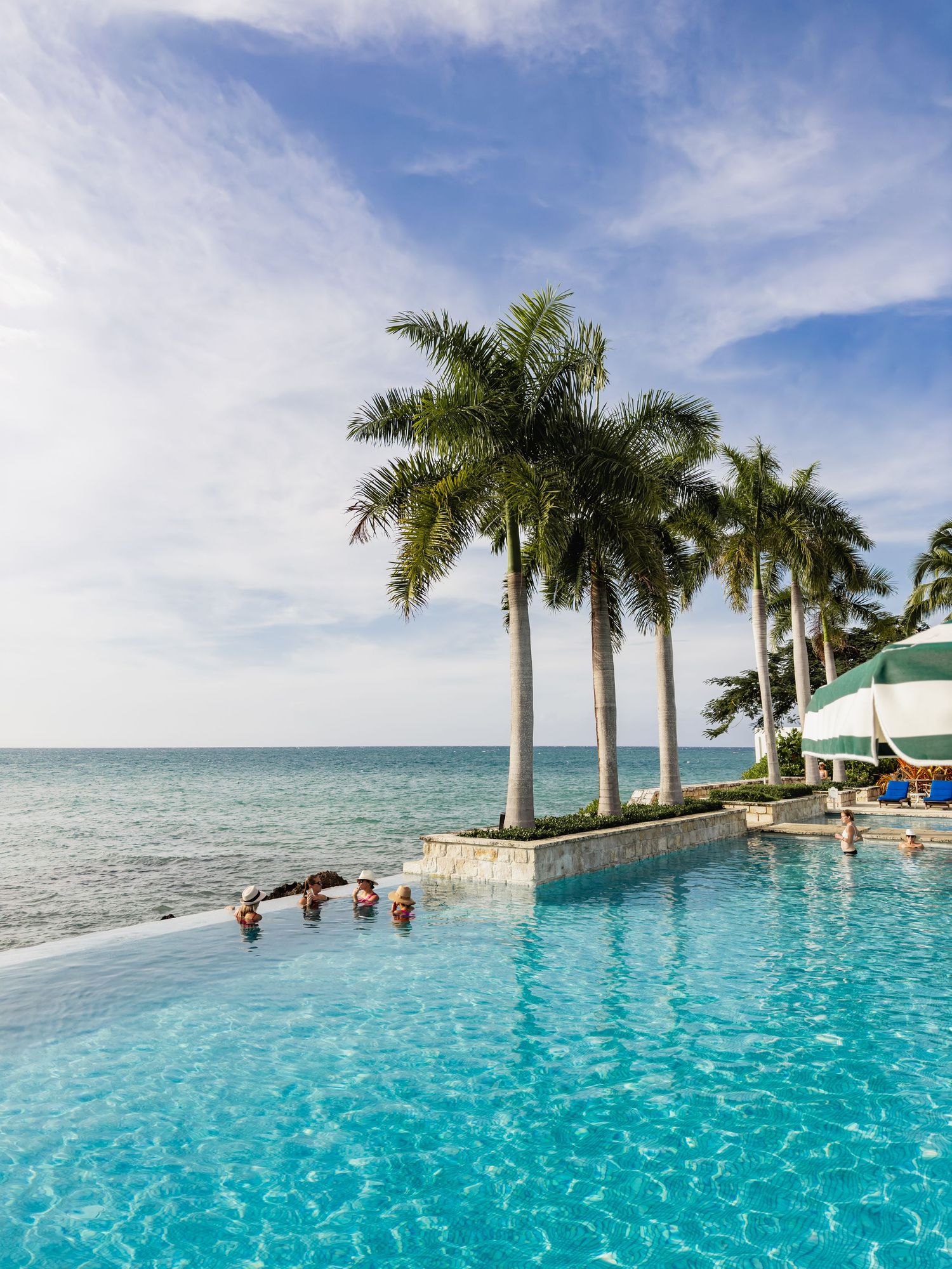 Luxurious infinity pool overlooking the ocean with palm trees and blue sky at a tropical resort destination.