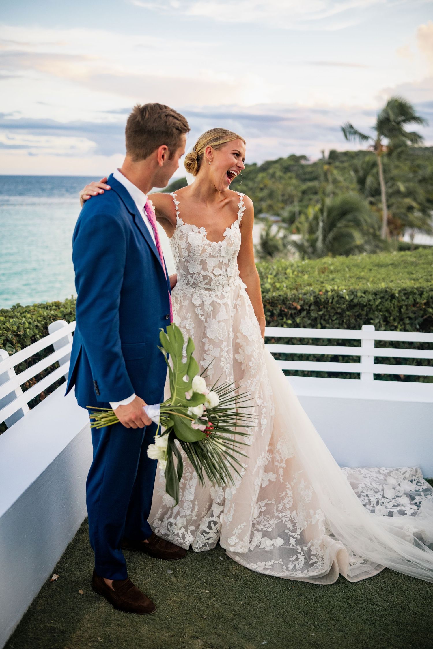 Wedding couple poses for romantic photos on a white balcony overlooking tropical ocean scenery.