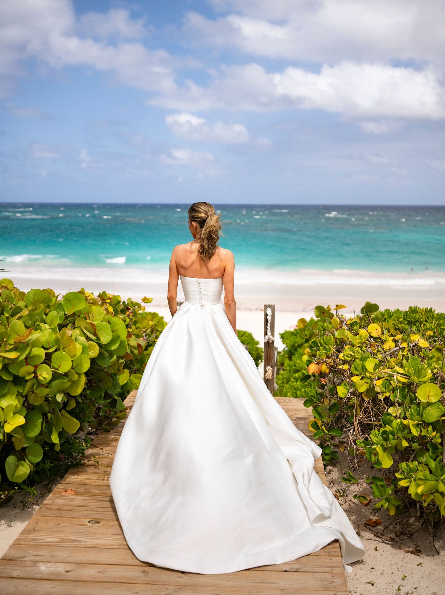 Bride in elegant white ballgown looks out over tropical beach with turquoise waters of harbour island Bahamas