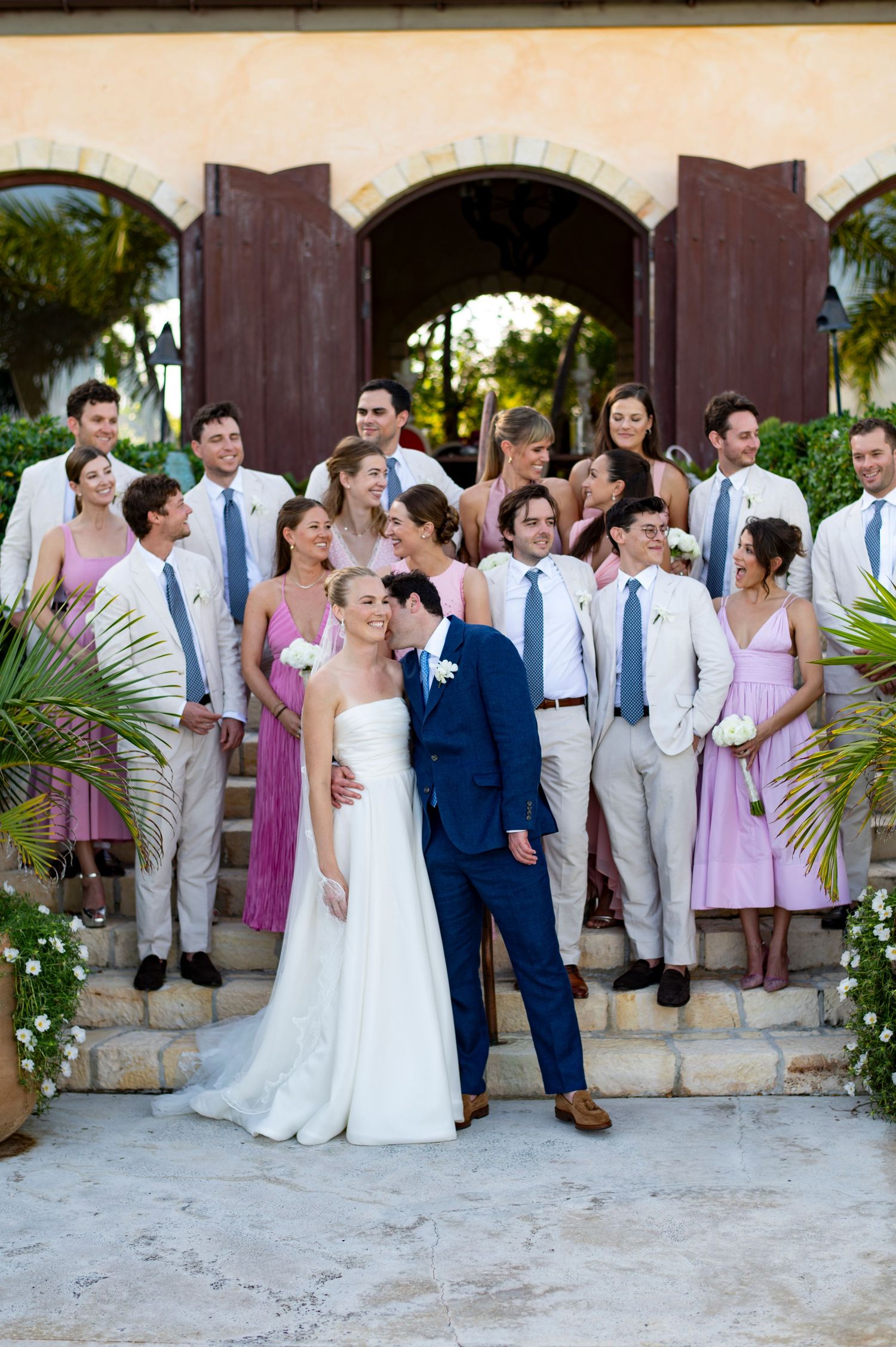 Wedding party in pink dresses and light suits gathered under Mediterranean-style archways.
