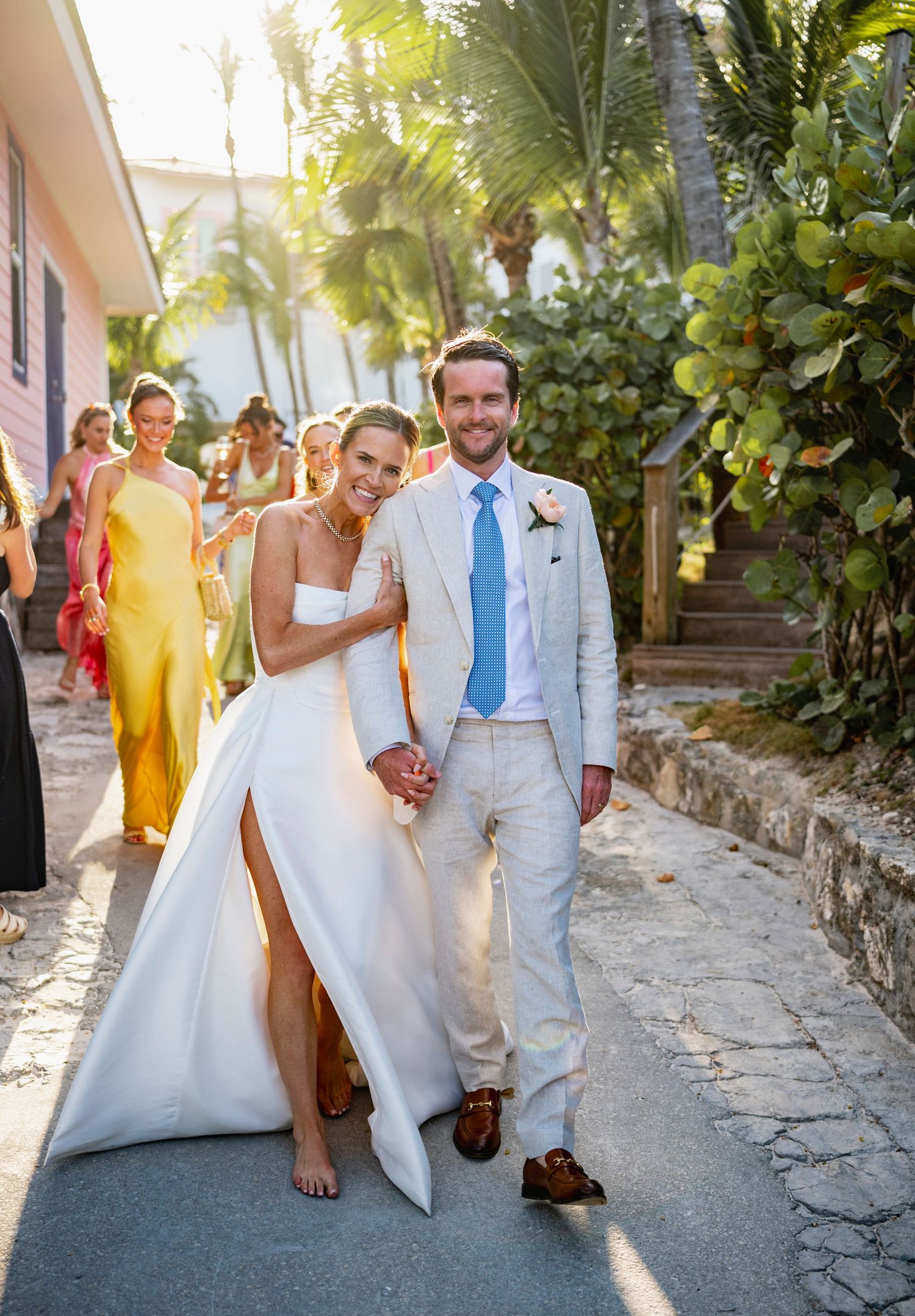 Wedding party walking along a tropical pathway in white attire during a destination celebration.