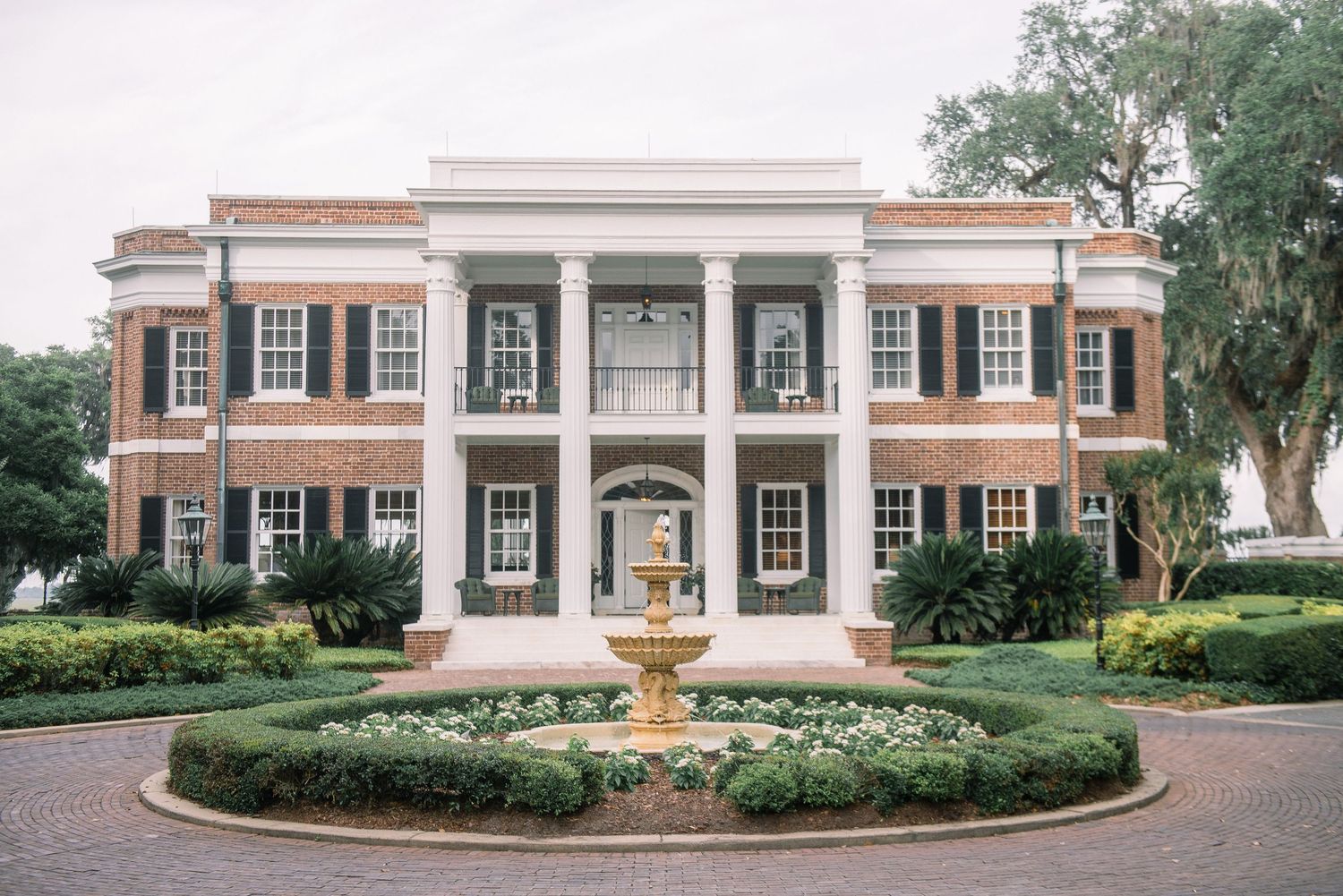 A panoramic view of a grand colonial-style brick building with white columns and manicured landscaping.