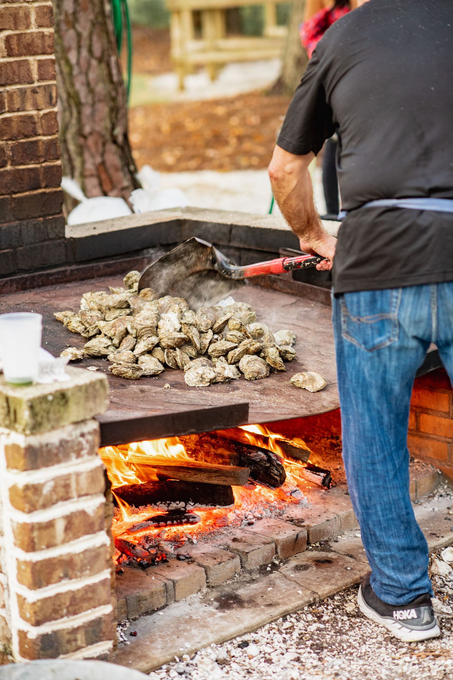 Fresh oysters being roasted on an outdoor brick fire pit with glowing embers and flames.