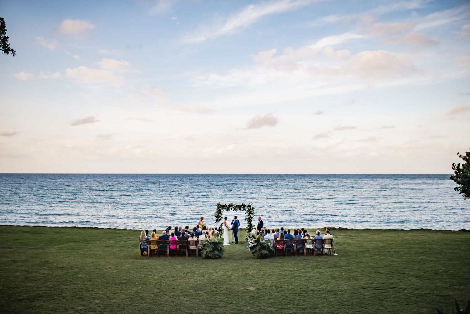 A panoramic view of a beach gathering with people and chairs set up along the shoreline at sunset.