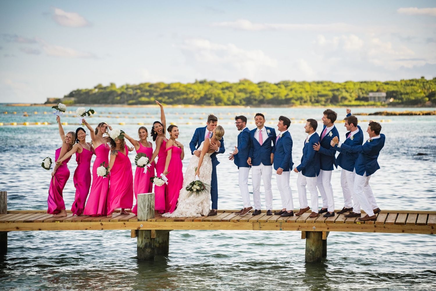 Wedding party members standing in ocean water wearing coordinated pink and navy attire.