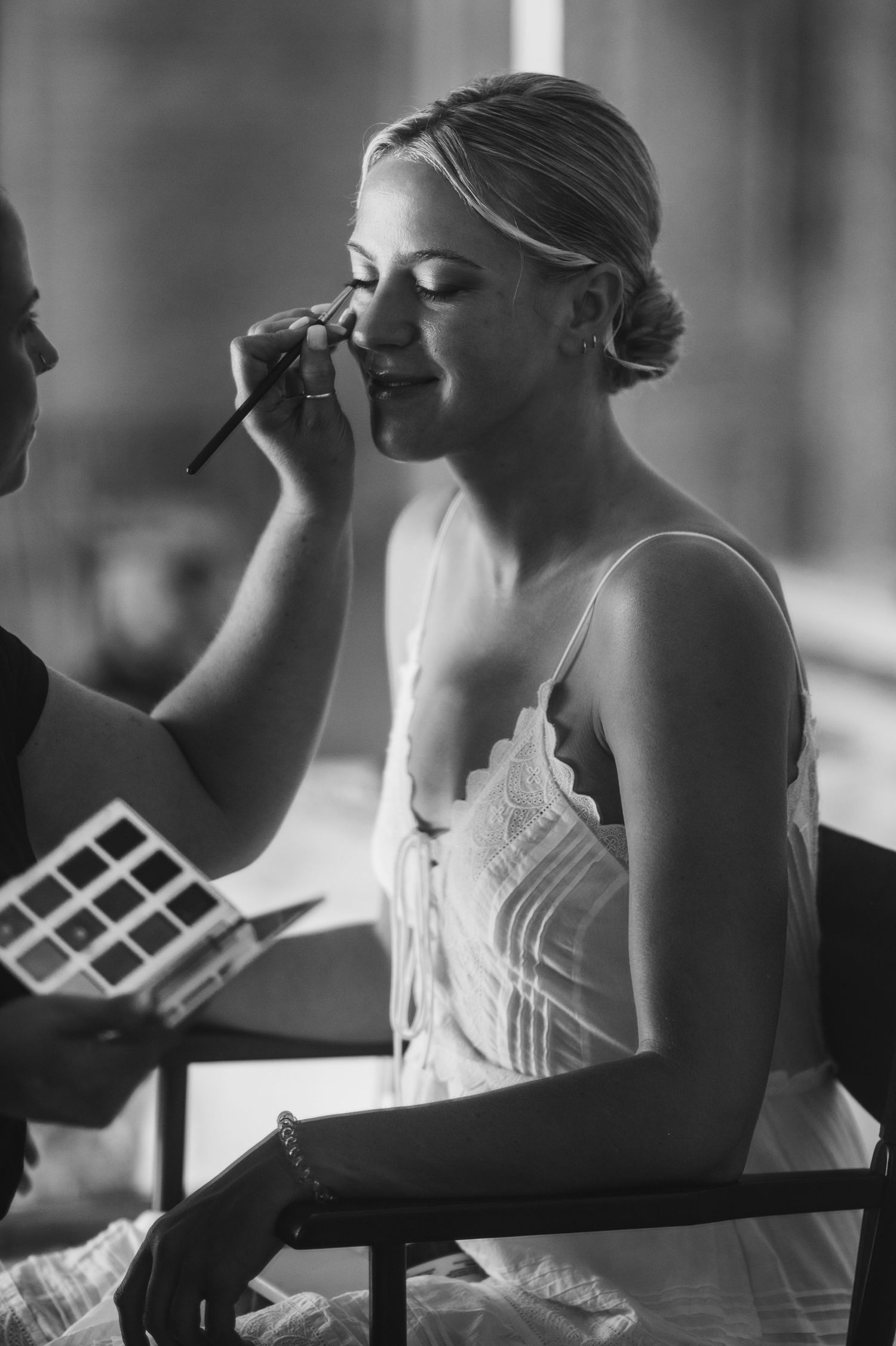 Black and white photo of bridal makeup application in a serene getting-ready moment.