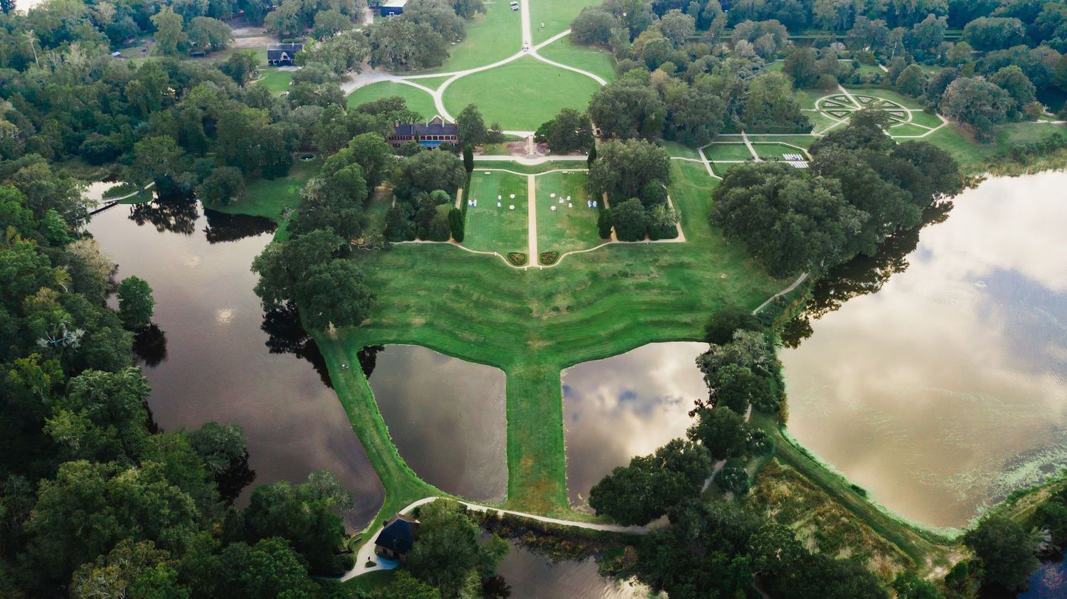 Aerial panoramic view of a lush green golf course with winding paths, water hazards and tree-lined fairways.