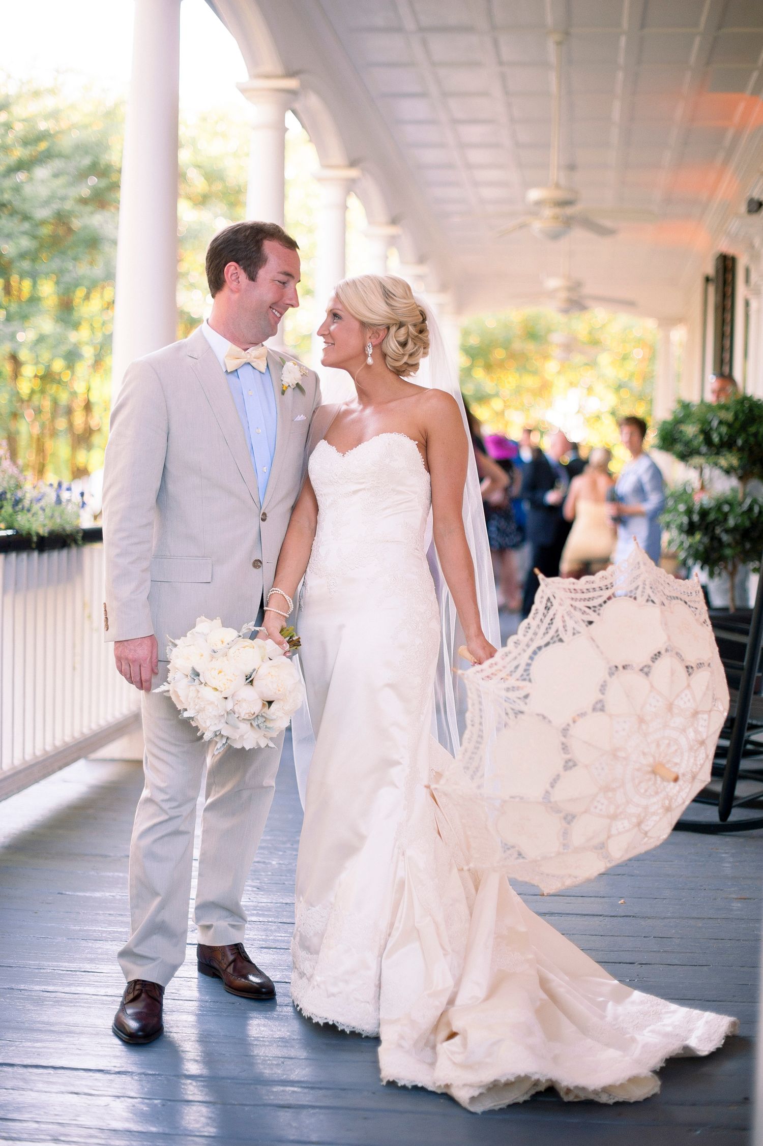 A romantic wedding couple shares a moment on an elegant porch, with the bride holding a white bouquet.