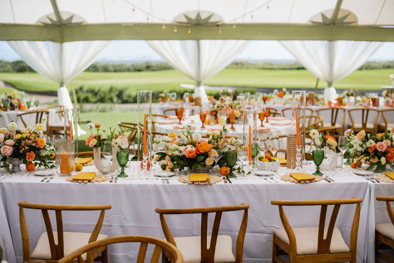 Elegant outdoor wedding reception setup with wooden chairs and floral centerpieces under white tent canopy.