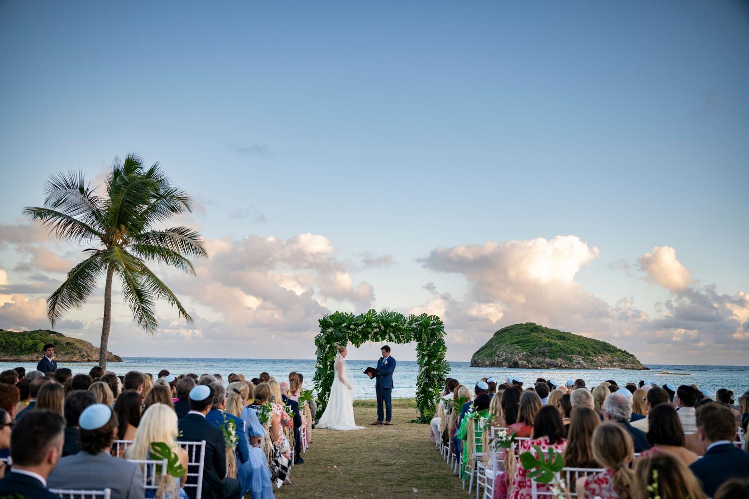Panoramic view of a beach wedding ceremony setup with palm trees and ocean views.