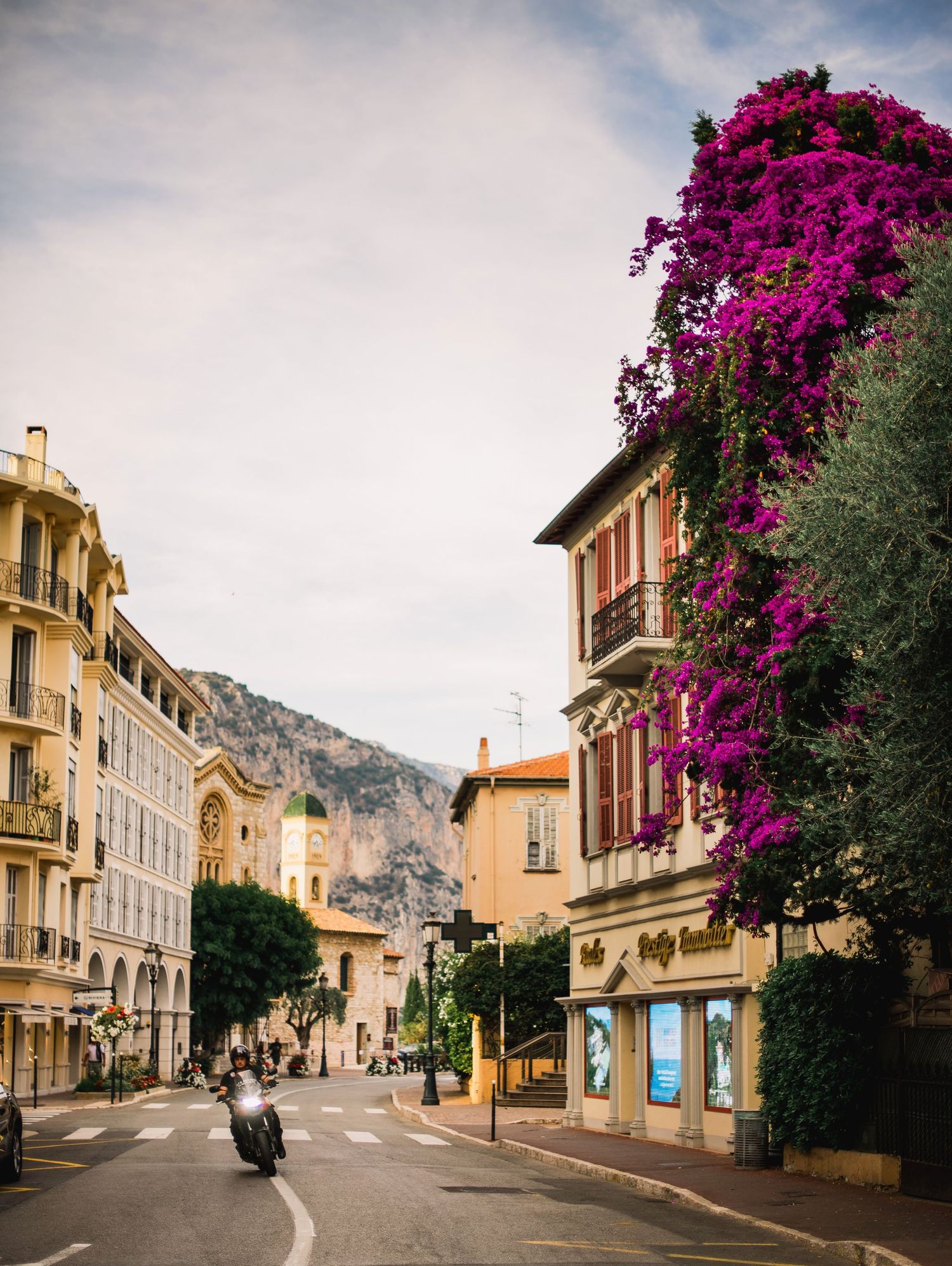 Charming European street in Beaulieu Sur Mer with vibrant pink bougainvillea and historic buildings.