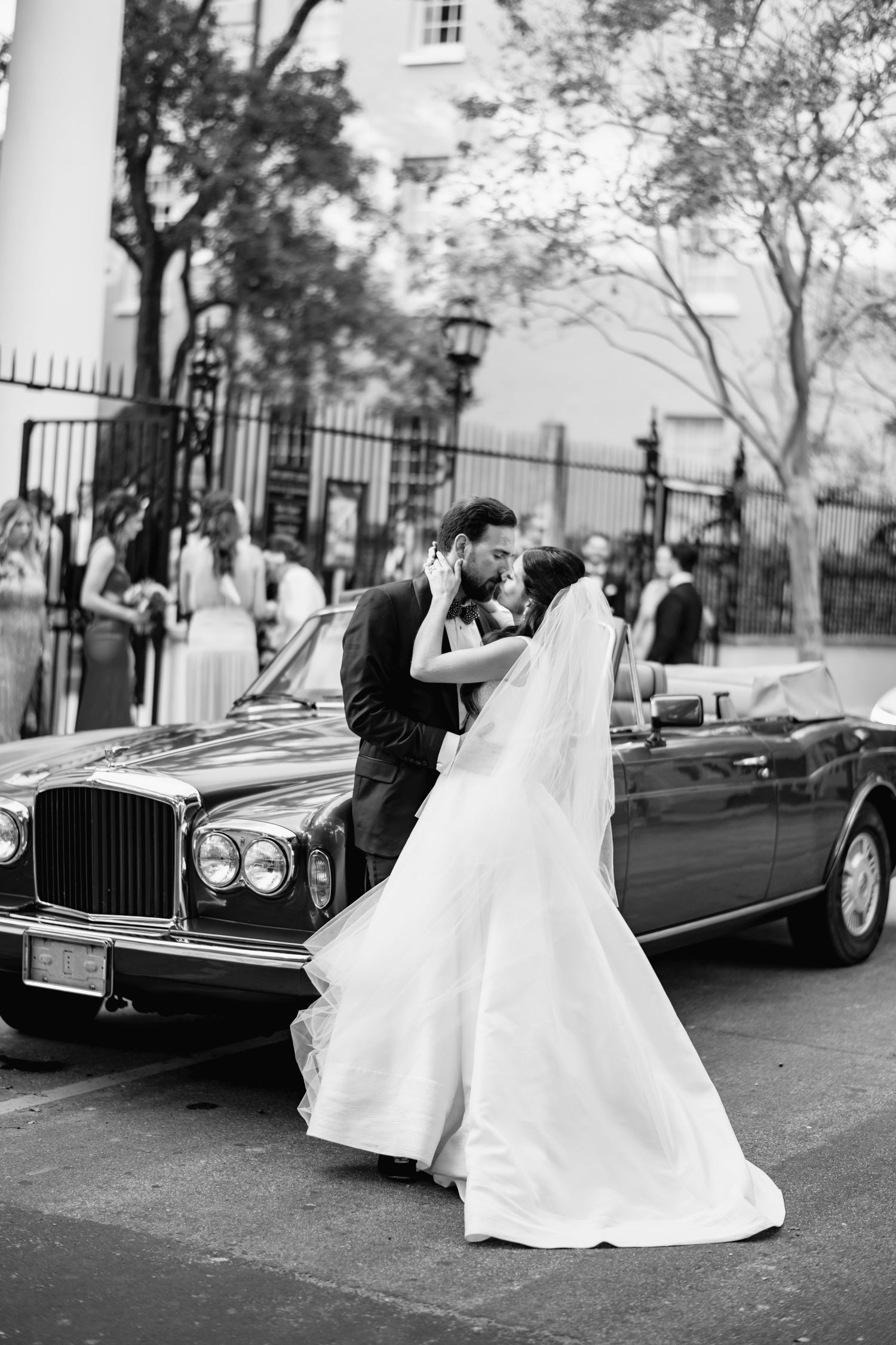 Black and white photo series of newlyweds posing with classic car on city street.