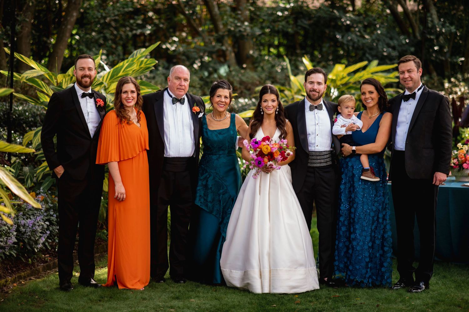 Wedding party poses together in a garden setting wearing formal attire in shades of blue and orange.