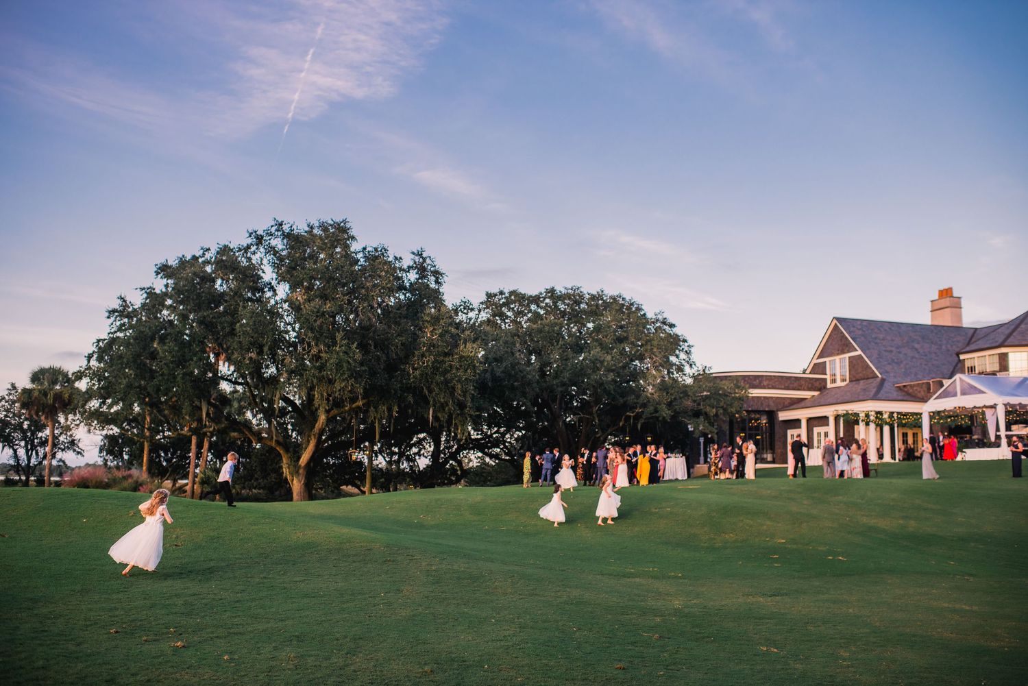 A panoramic view of a golf course with trees and buildings in the background under a blue sky.