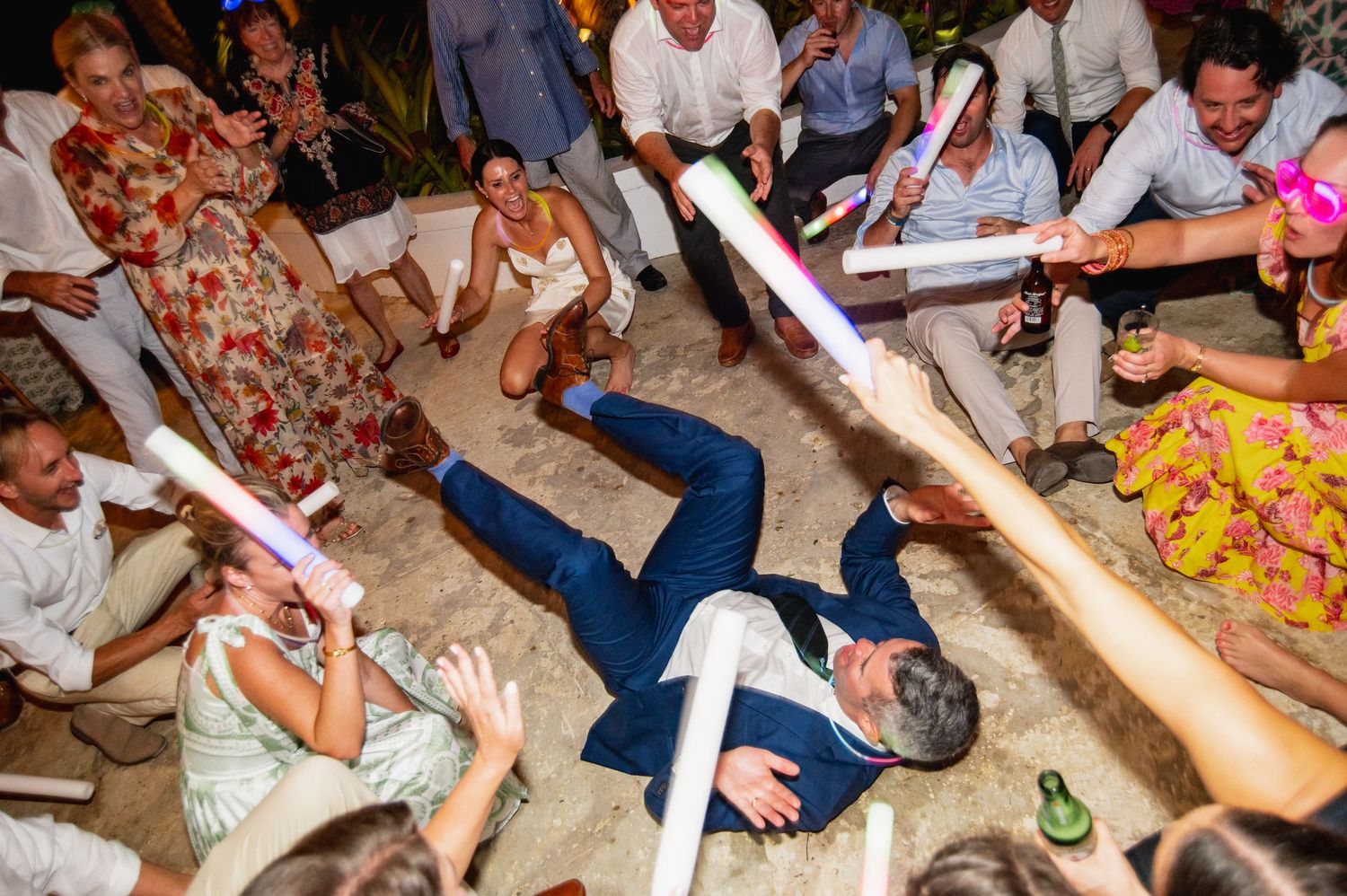 A group of people sitting on the floor enjoying a party with drinks and snacks in a casual indoor setting.