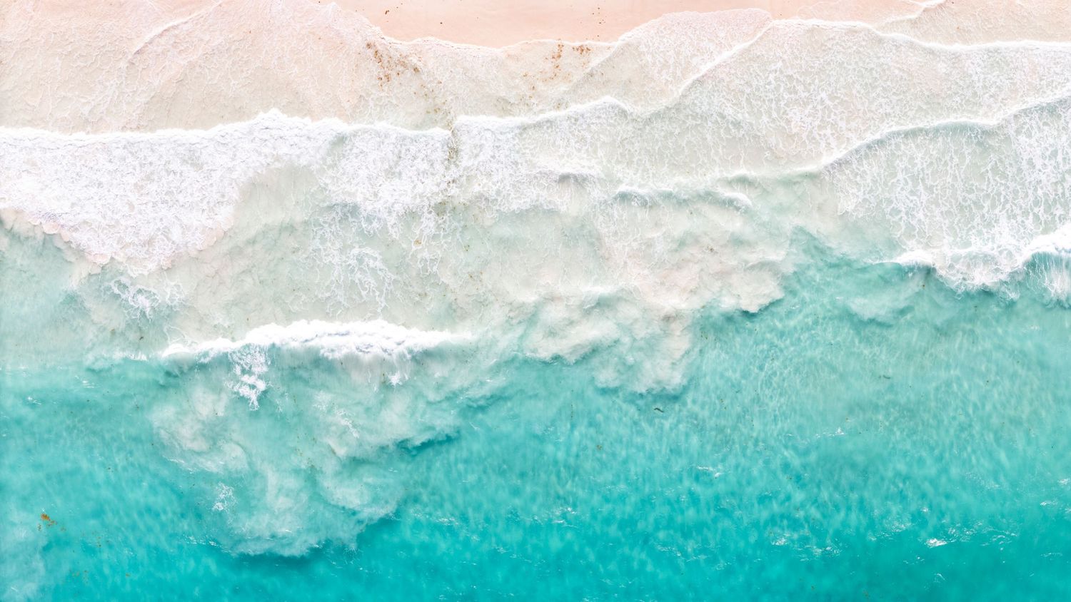 Aerial view of turquoise ocean waves meeting white sandy beach with crystal clear waters.