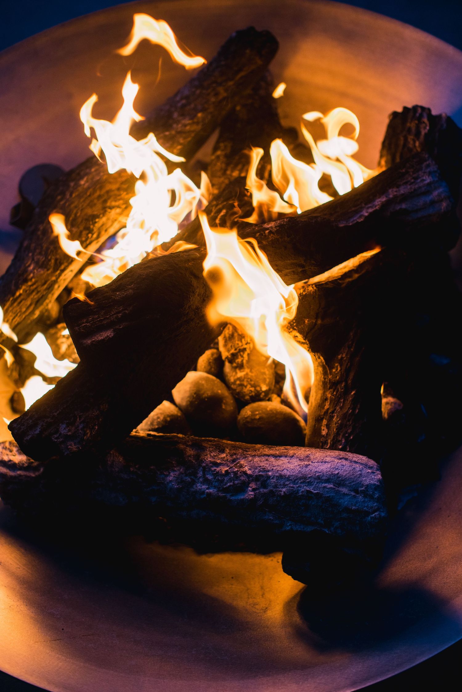 Close-up shots of burning logs in a fire pit showing bright orange flames against a dark background at night.
